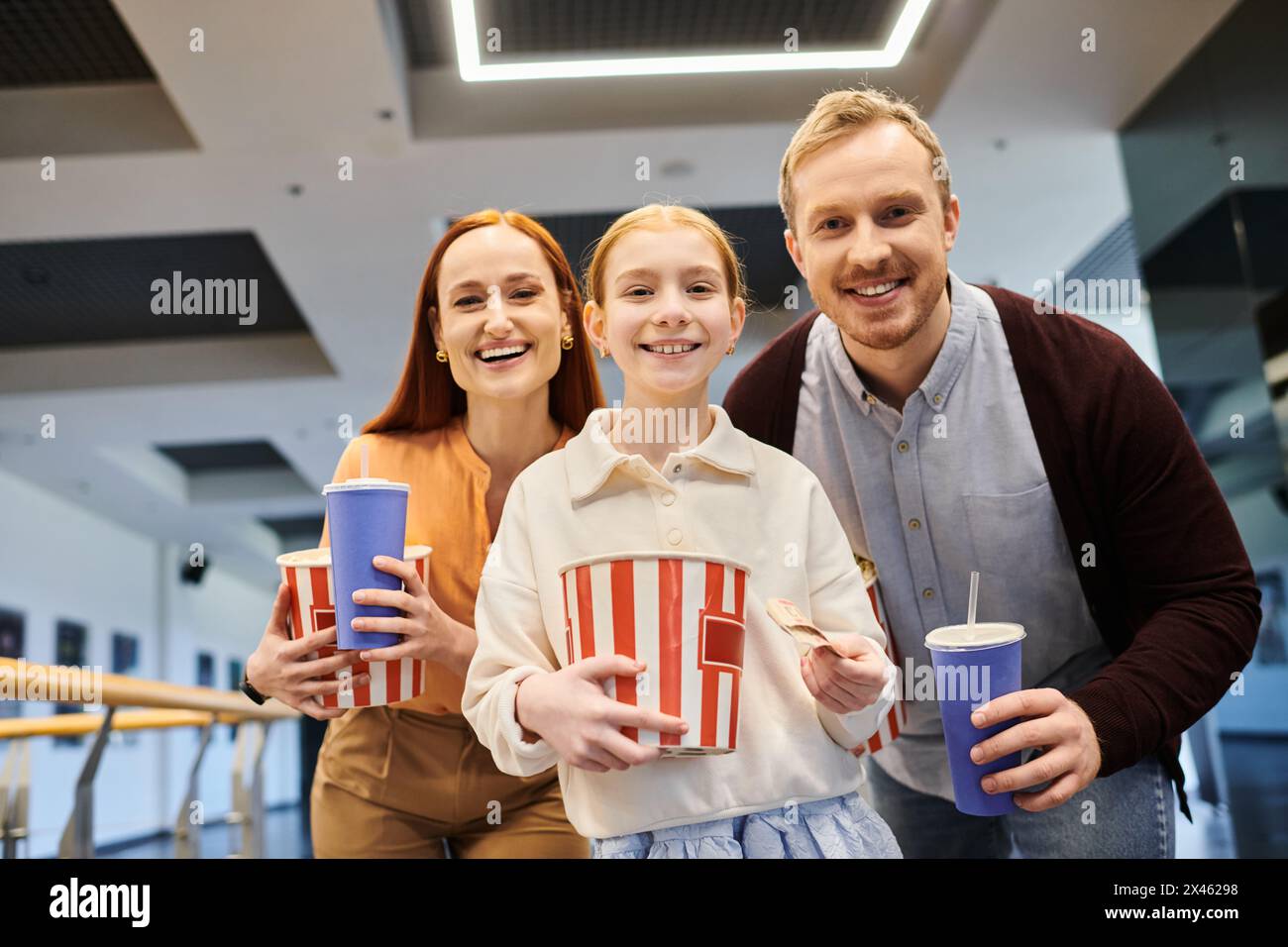 family smiling, holding cups of popcorn, bonding and enjoying a fun movie time together at the cinema. Stock Photo