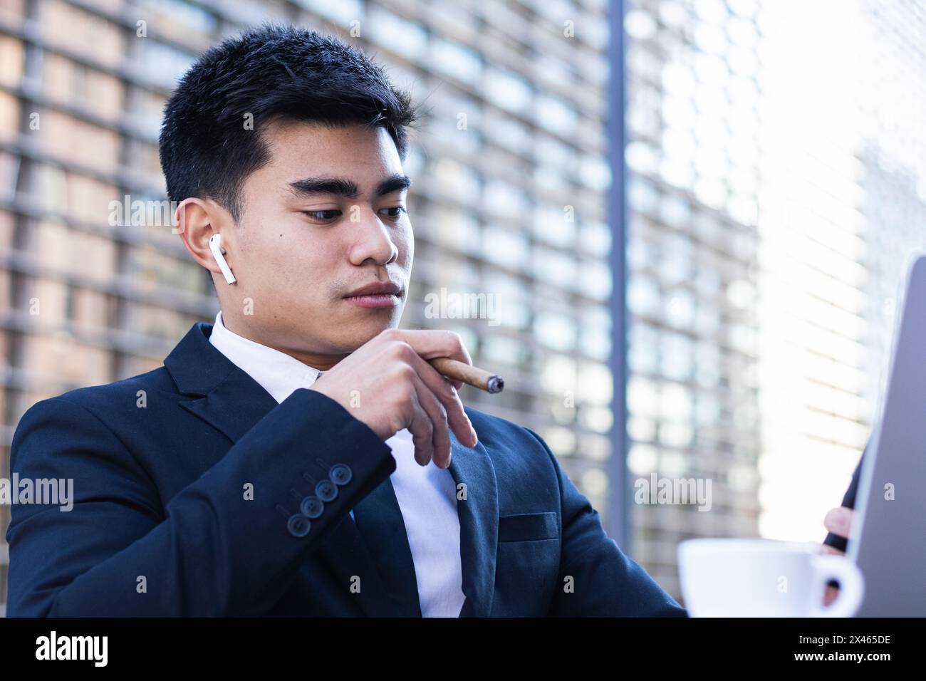 Confident Asian male entrepreneur sitting at table in cafe and smoking cigar while browsing smartphone Stock Photo
