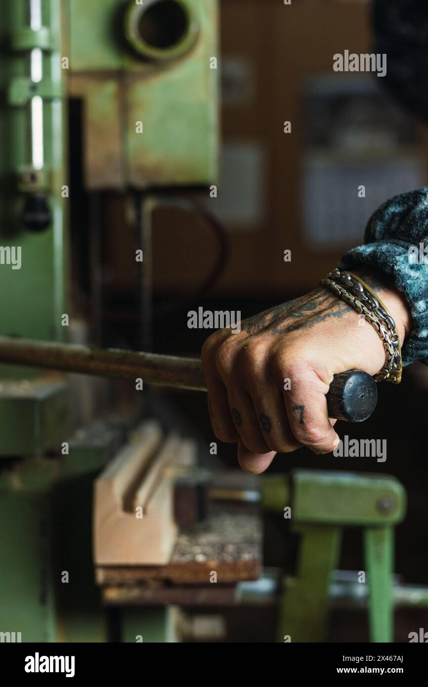 Crop unrecognizable tattooed male carpenter drilling wooden board using lathe during work in joinery Stock Photo