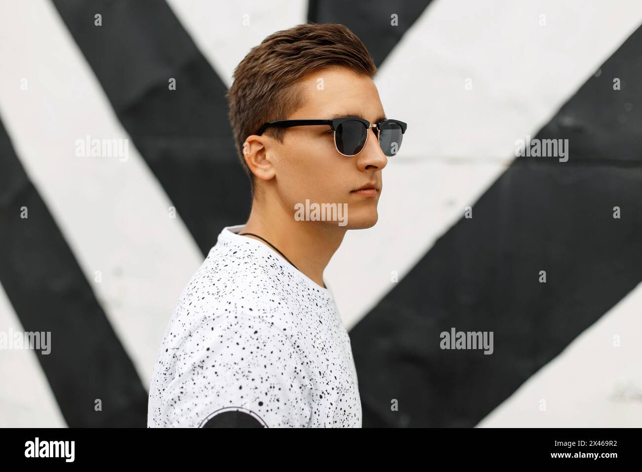 Young Handsome Guy With A Hairstyle And Sunglasses On A Background Of Black And White Stripes. Stock Photo