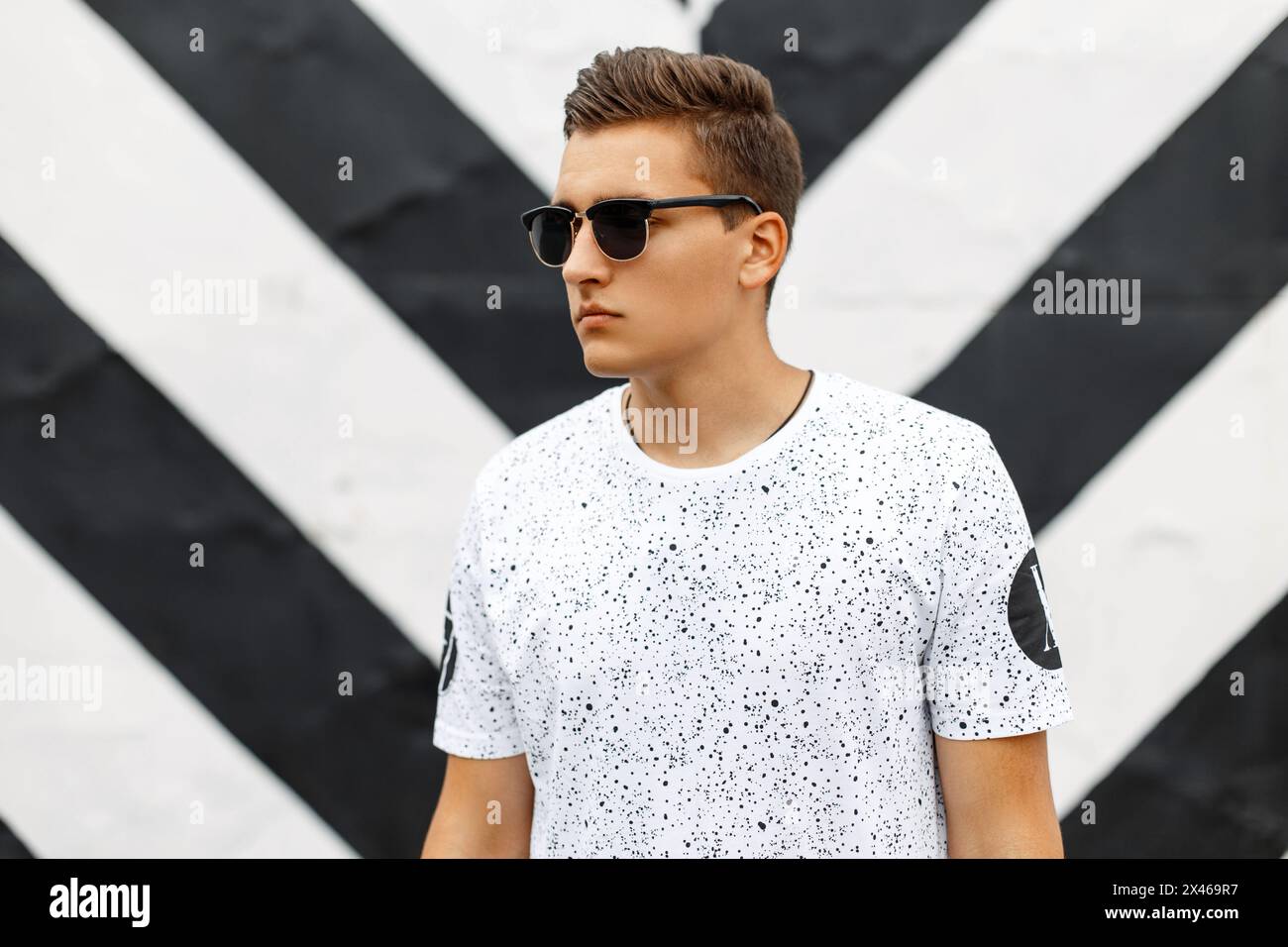 Handsome Man In Sunglasses And A White T-shirt With Spots On A Background Of Black And White Lines. Stock Photo