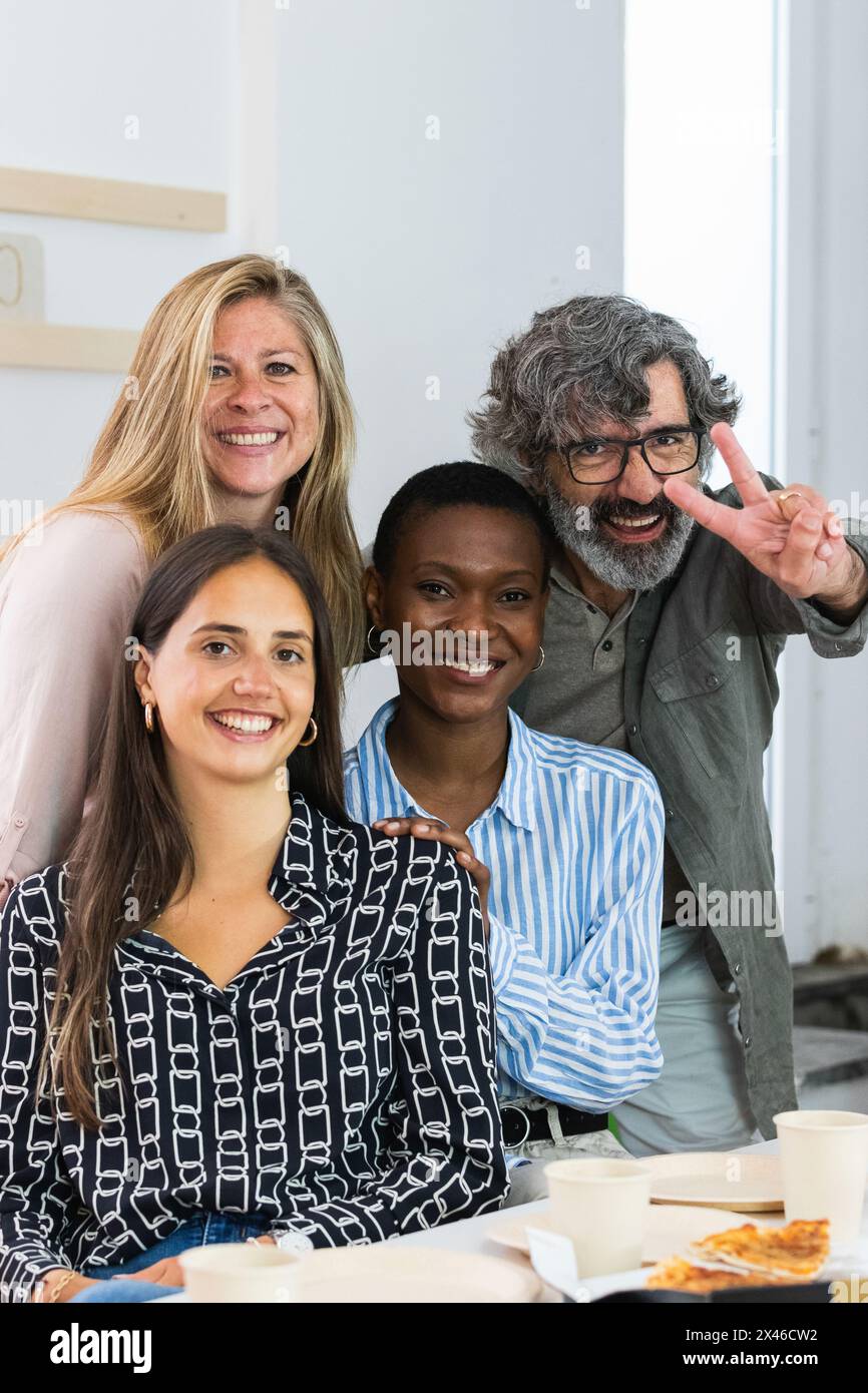 Delighted multiracial female colleagues looking at camera and smiling while sitting in workplace together Stock Photo