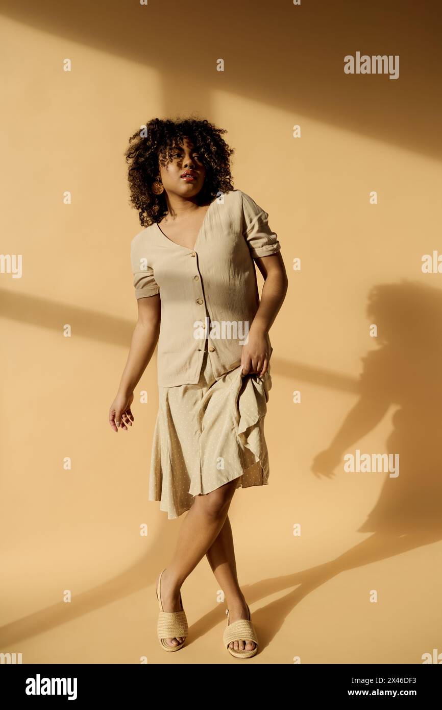 A beautiful young African American woman with curly hair stands in a room, casting a striking shadow on the wall. Stock Photo