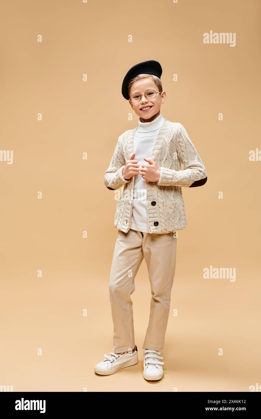 A young boy in a white shirt and tan pants poses as a film director against a beige backdrop. Stock Photo
