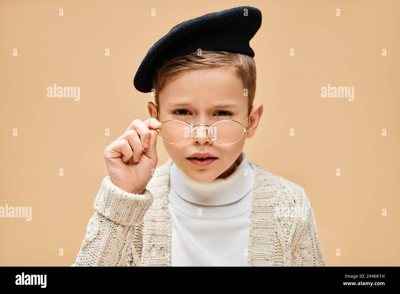 Preadolescent boy in glasses and hat, dressed as a film director on a beige backdrop. Stock Photo