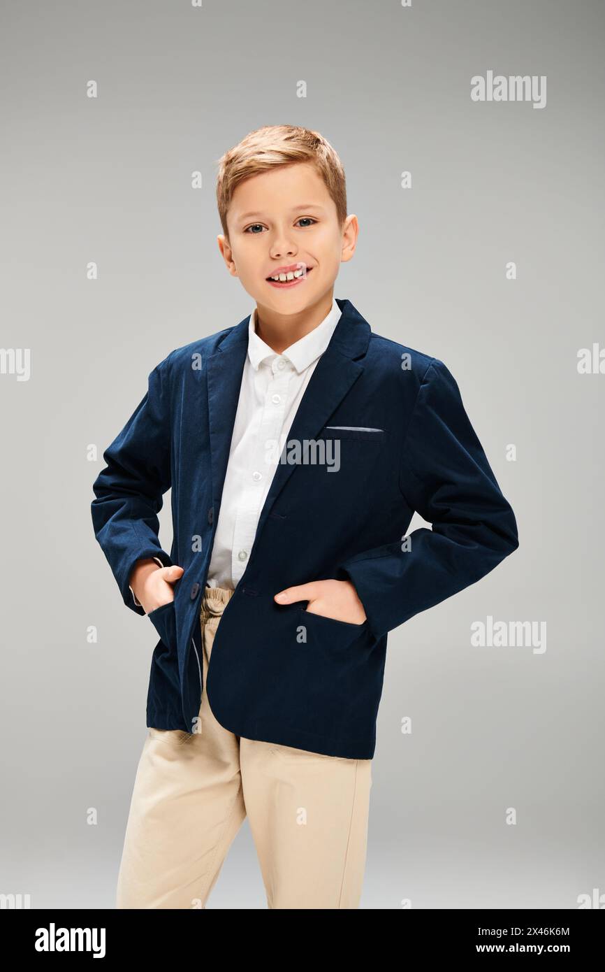A young boy dressed in a stylish blue jacket and tan pants, exuding elegance on a gray backdrop. Stock Photo