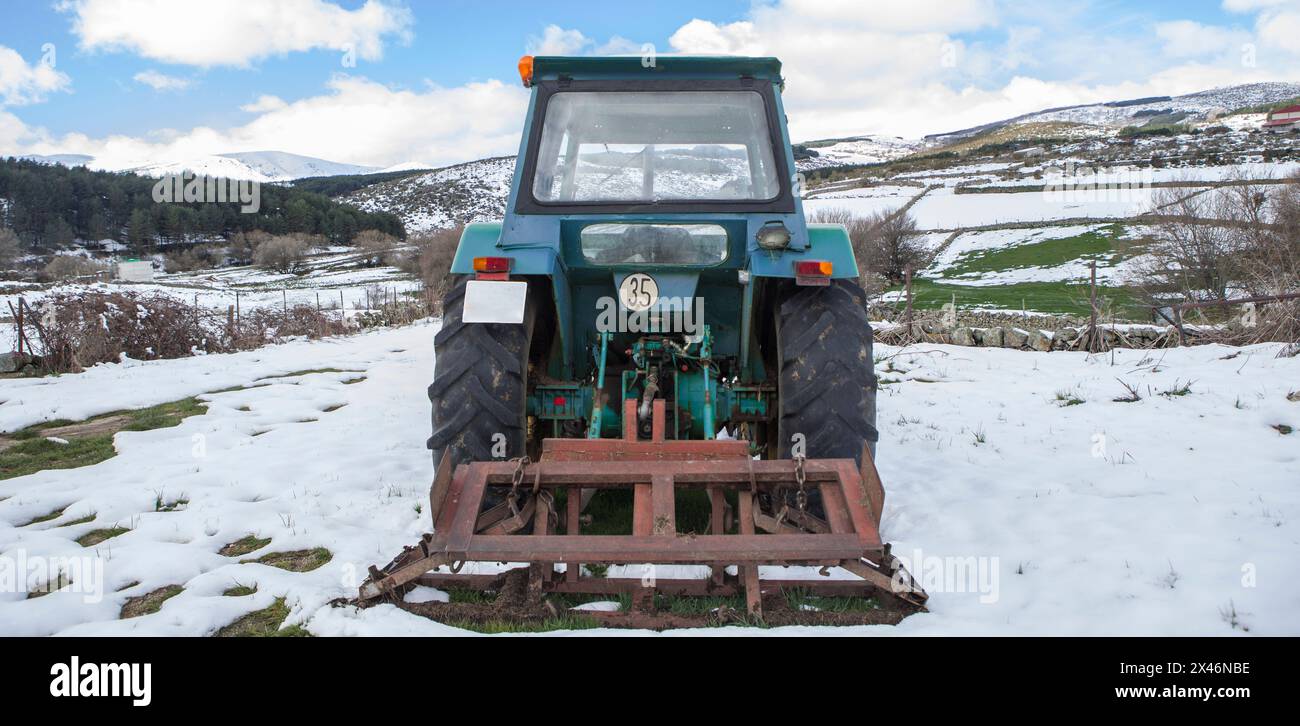 Old tractor equipped with implement parked in the middle of a snowy meadow. Mountain agriculture concept Stock Photo