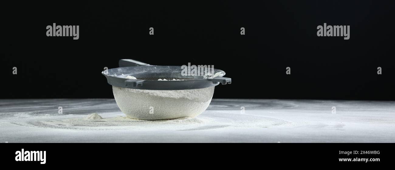 Sieve with flour on table against black background, space for text ...