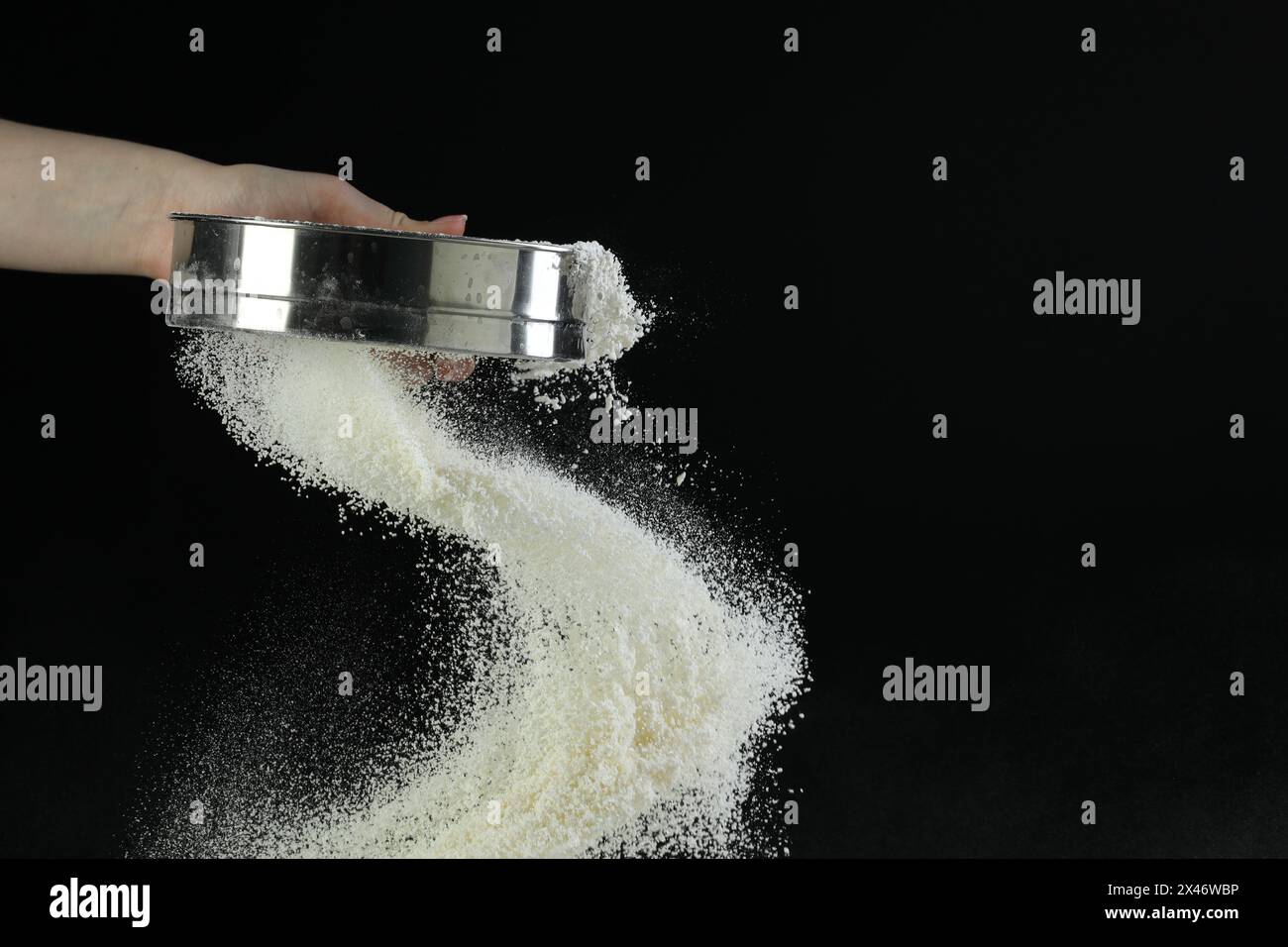 Woman sieving flour against black background, closeup. Space for text ...