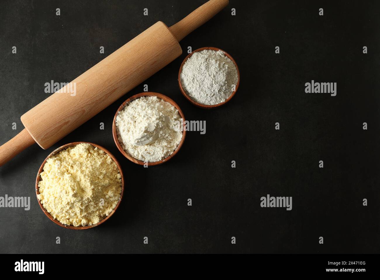 Rolling pin and different types of flour on black table, flat lay ...