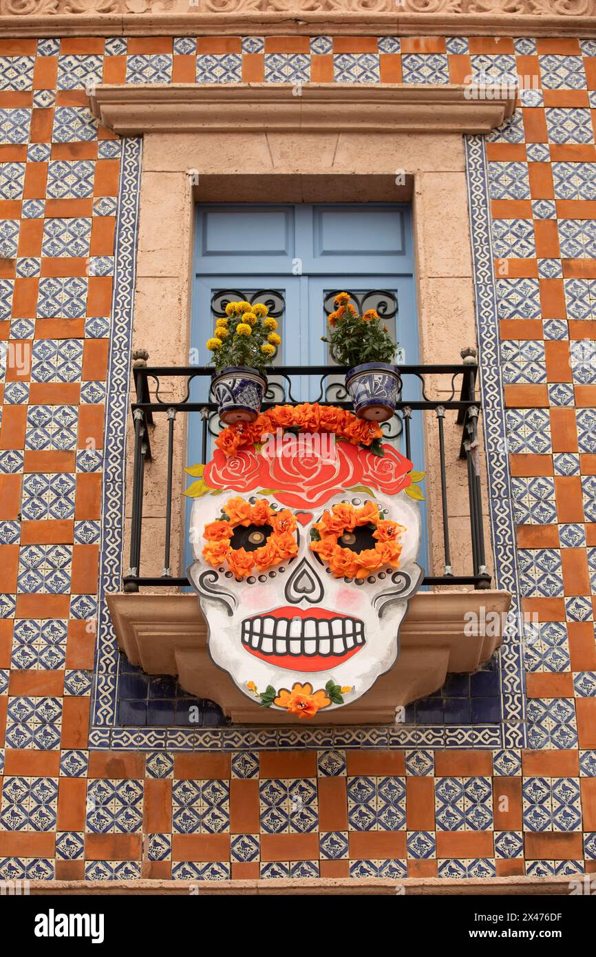 Bernal, Querétaro, Mexico - November 20, 2023: Día de los Muertos decorations hang outside of a tiled building's window. Stock Photo