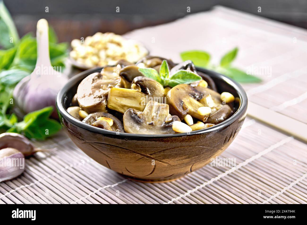 Champignons baked with oregano, wine, garlic, lemon and pine nuts in bowl on brown bamboo napkin on wooden board background Stock Photo