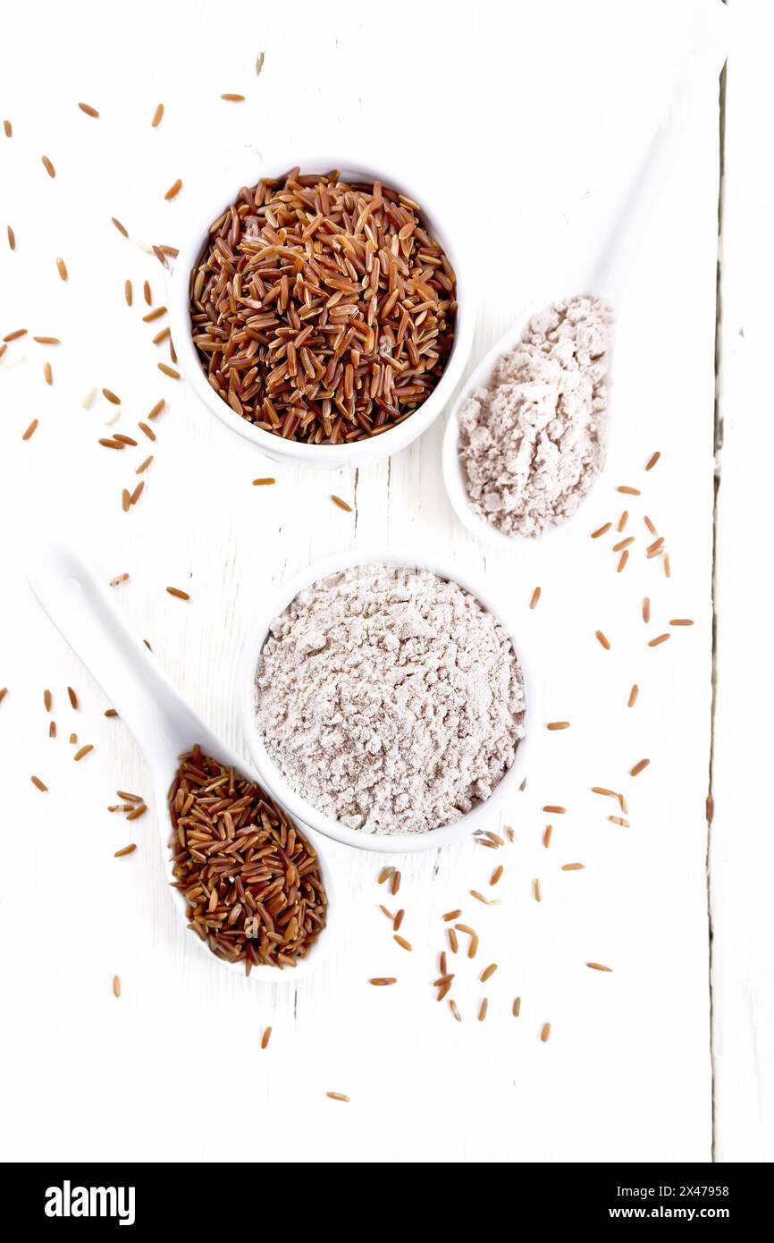 Red rice flour in bowl and spoon, cereal in spoon, bowl and on table against the background of light wooden board from above Stock Photo