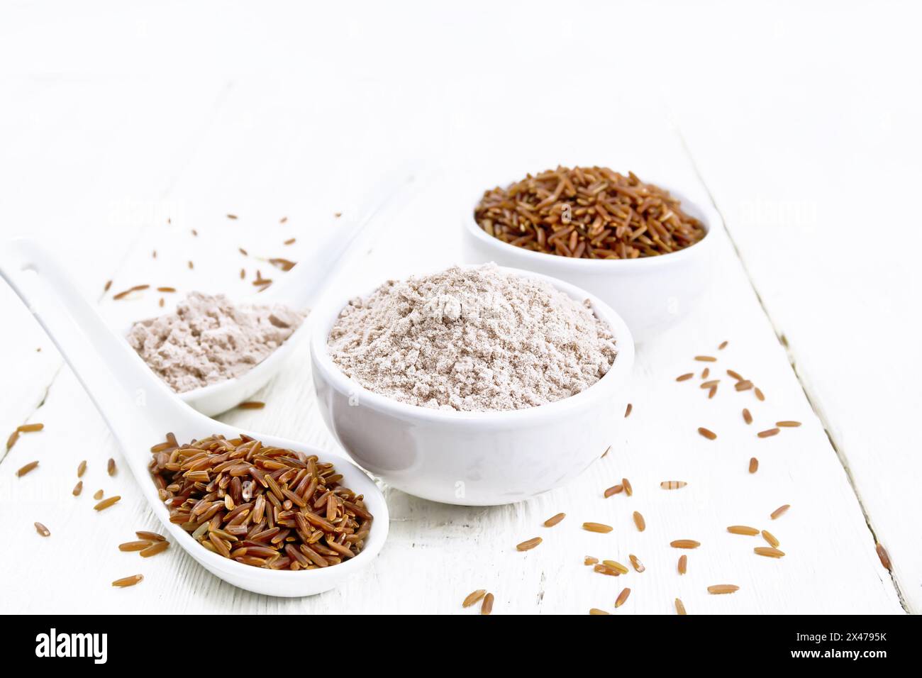 Red rice flour in bowl and spoon, cereal in spoon, bowl on wooden board background Stock Photo