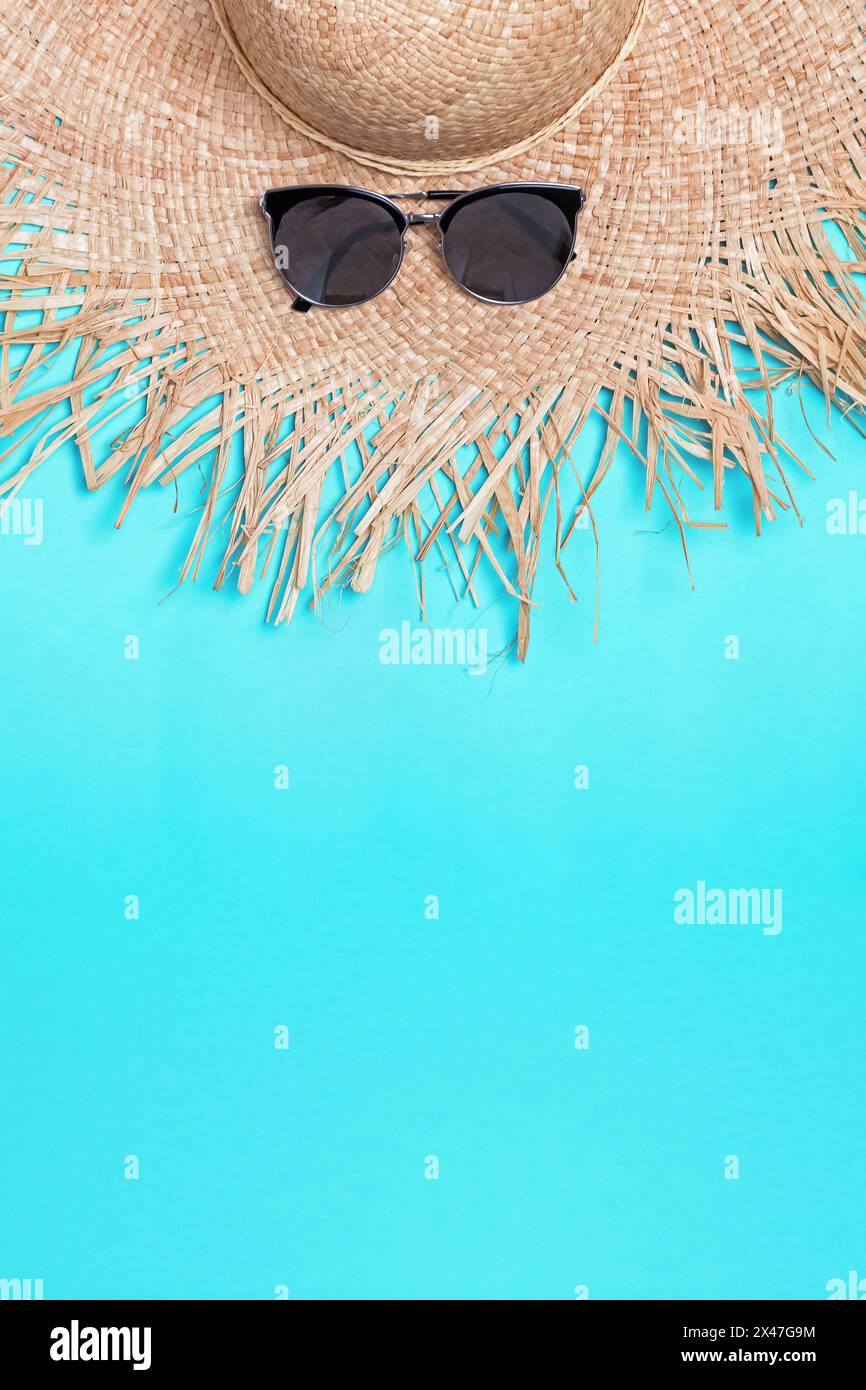 Straw hat with wide fields and sunglasses on blue background with copy space Stock Photo