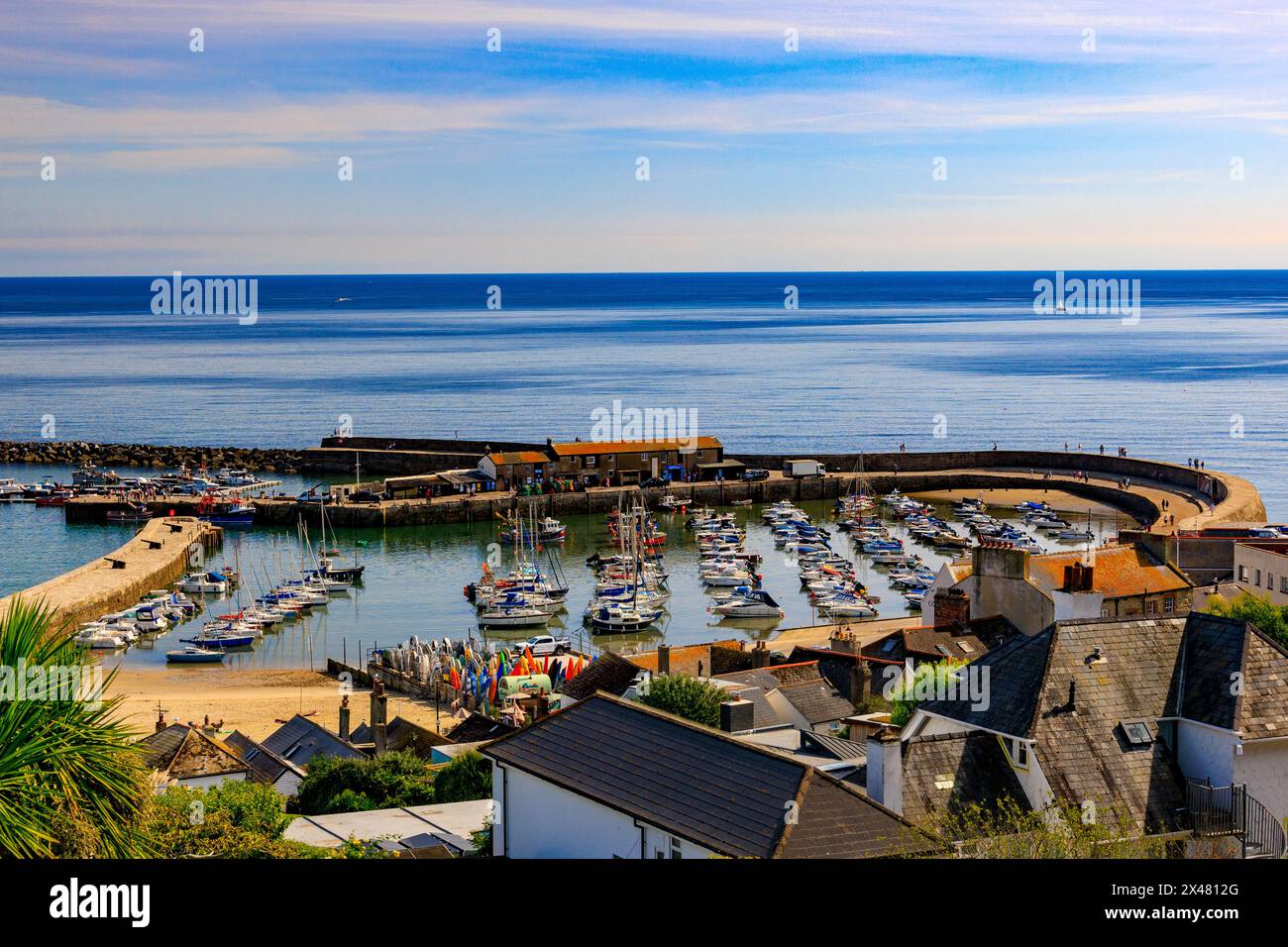 Lyme Regis harbour and The Cobb at high tide with a colourful selection of boats and surfboards visible, Jurassic Coast, Dorset, England, UK Stock Photo