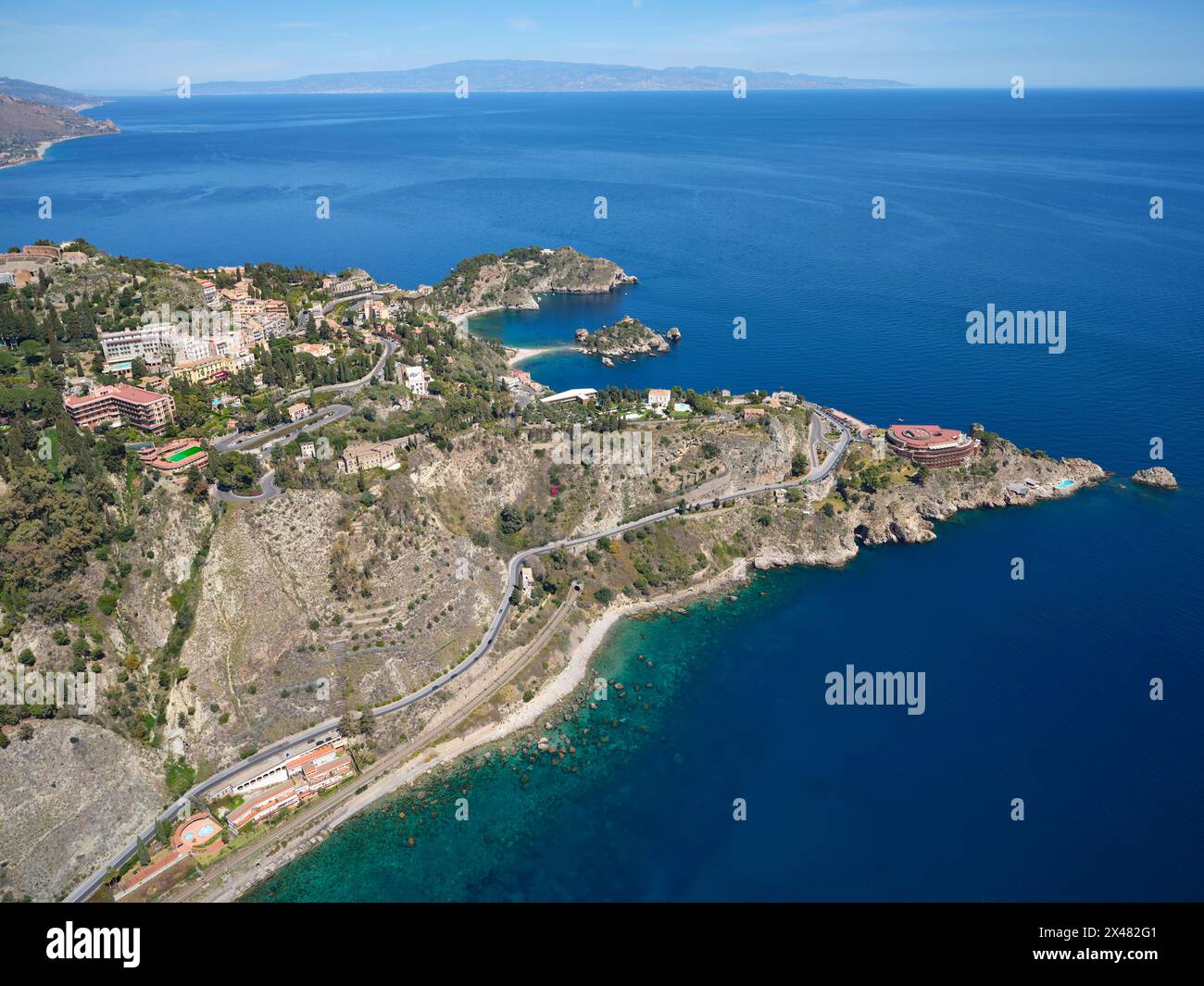 AERIAL VIEW. The rocky promontories of Taormina jutting out into the Ionian Sea. Metropolitan City of Messina, Sicily, Italy. Stock Photo