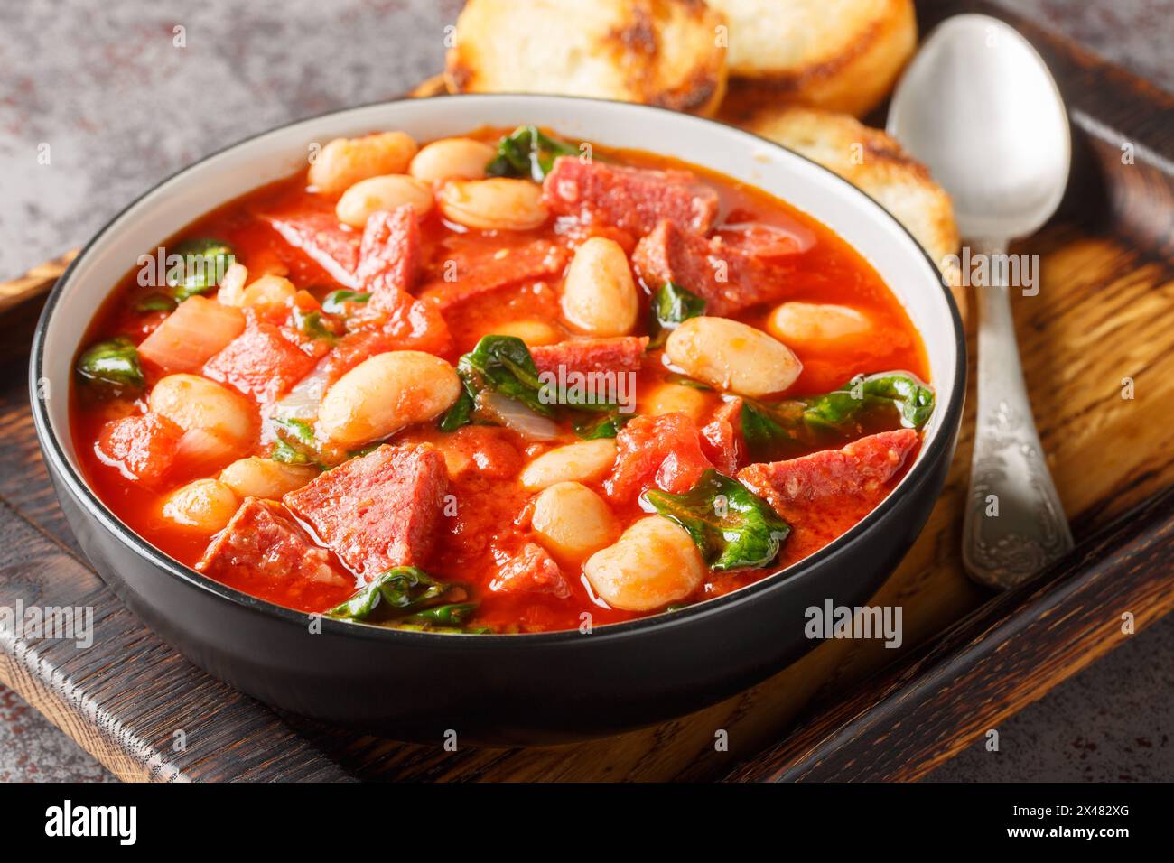 Spanish stew of butter beans, chorizo and spinach in tomato sauce close-up in a bowl on the table. Horizontal Stock Photo