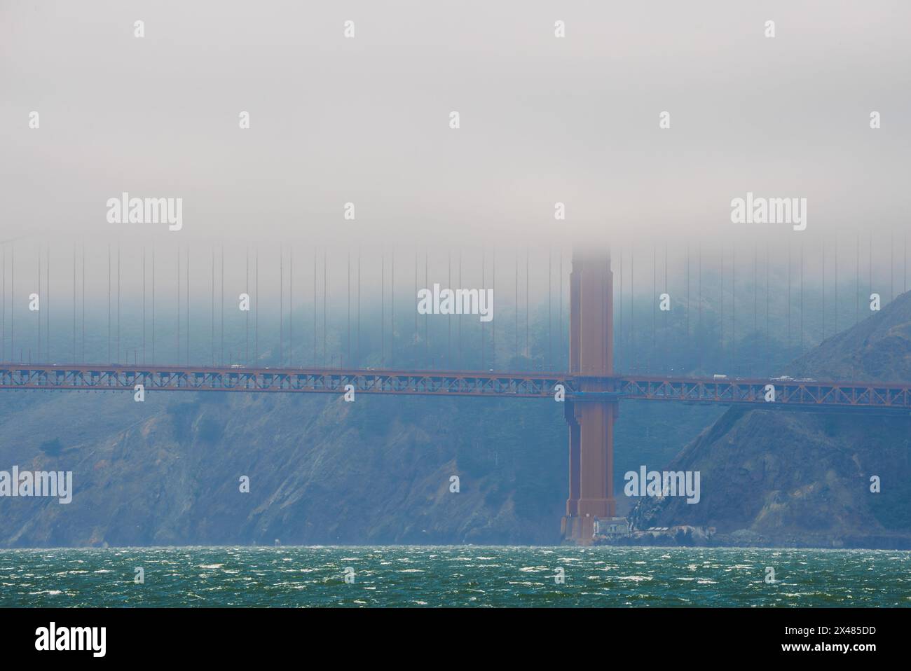 Iconic Golden Gate Bridge in fog, waters choppy, hinting the scale of ...