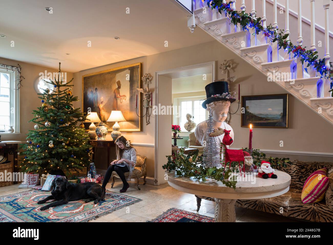 Girl sits with dog and Christmas tree in Dorset family home at Christmas, England, UK Stock Photo