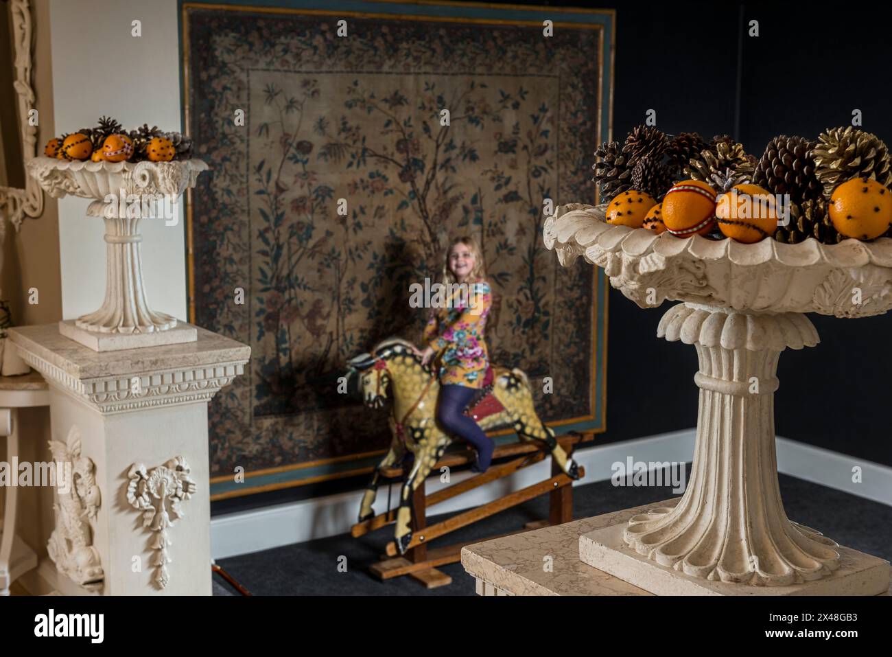 Girl on antique rocking horse and urns with fruit in Dorset family home at Christmas, England, UK Stock Photo