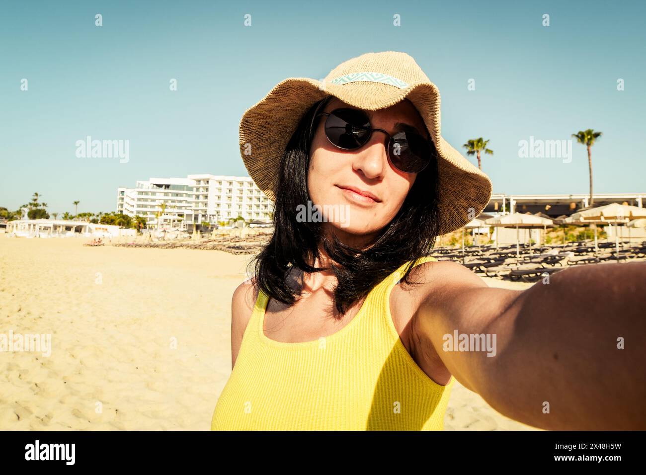 Satisfied adorable single female model is summer hat takes selfie travel solo in tropical island. Woman blogger shares news with followers Stock Photo