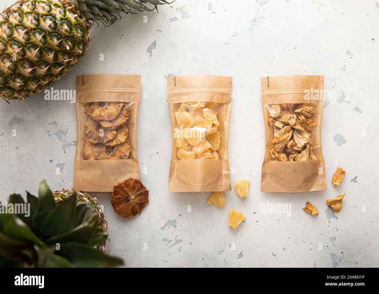 Packages with dried sweet pineapple slices and circles on light background with raw pineapple fruit. Stock Photo