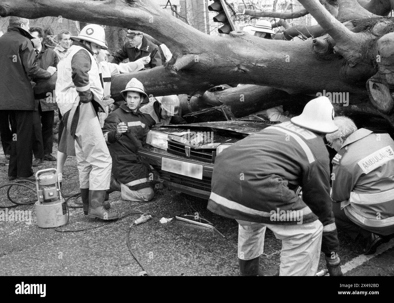An archive newspaper image of Fire crews and Poilce rushing to save a driver in a car partially crushed under a fallen tree during the great storm in January 1990. Stock Photo