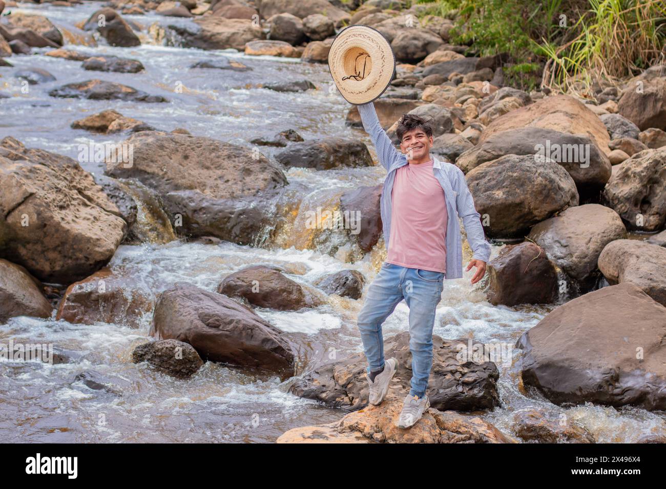 lifestyle. very happy young latin man on the rocks of the river waves with hat in hand Stock Photo
