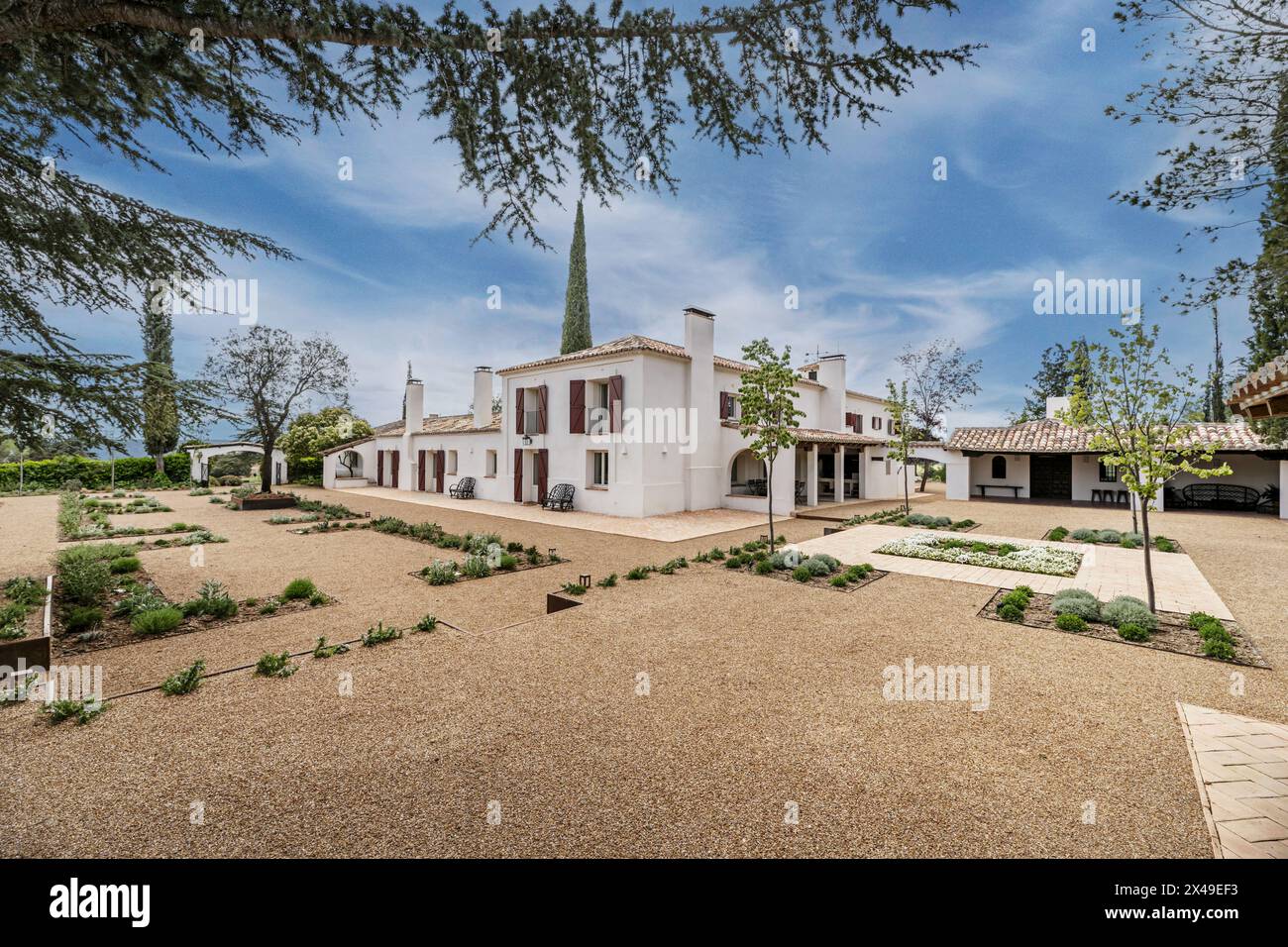 a beautiful Andalusian style country house with white walls, gravel paths and a variety of newly planted plants in the garden on a day with beautiful Stock Photo
