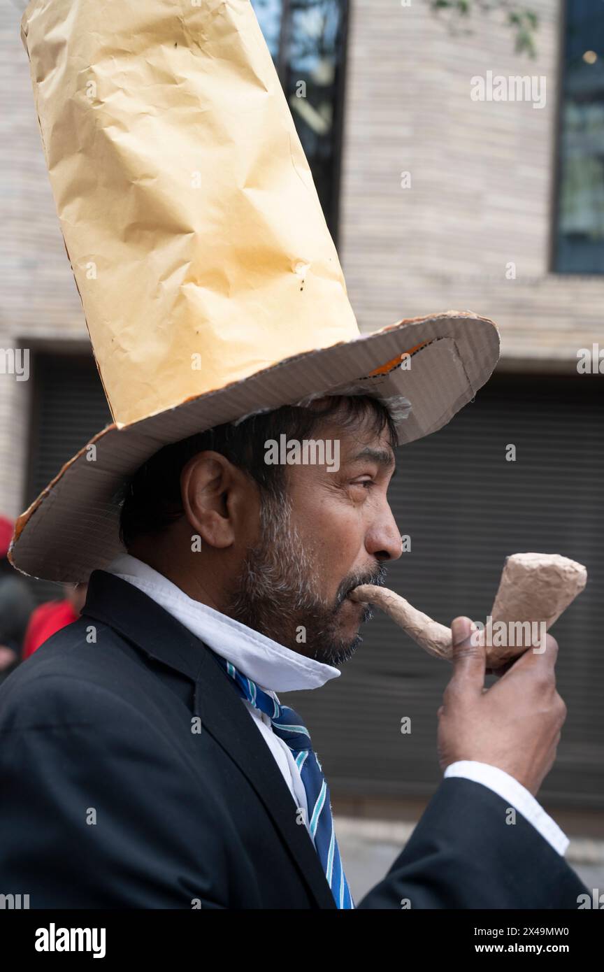 May 1st 2024. People assemble on Clerkenwell Green to march to Trafalgar Square to celebrate May Day. A man dresses as a caricature of a banker with t Stock Photo