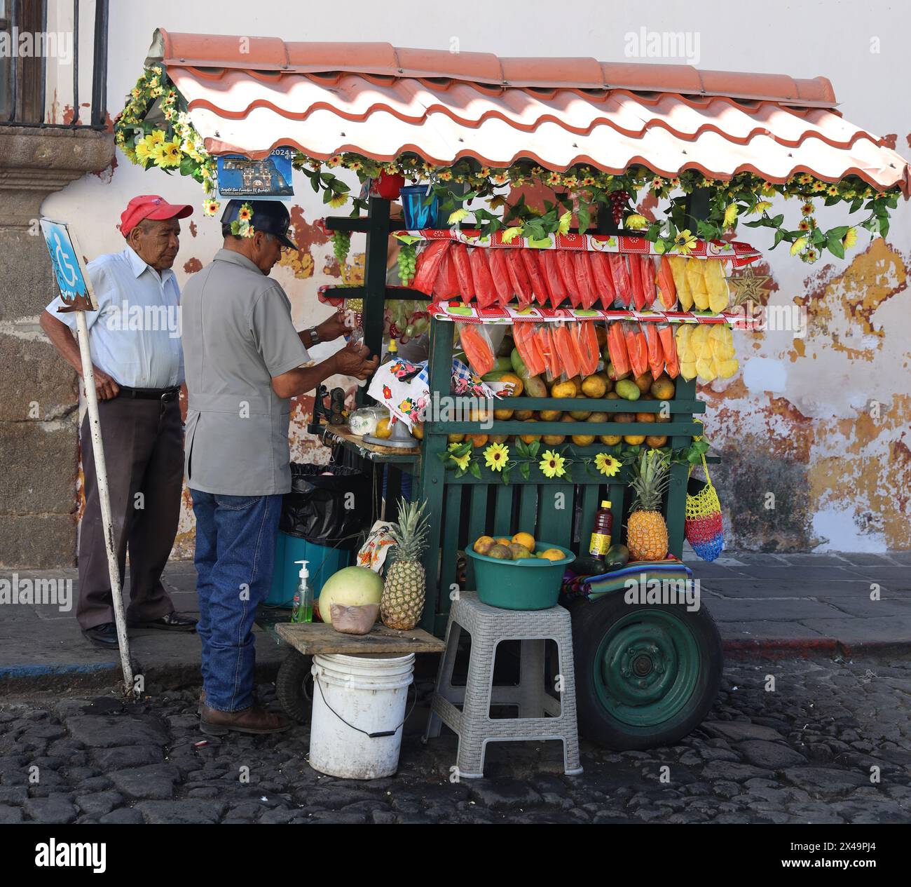 Fruit stall. Street seller, Antigua, Guatemala, Central America. Colourful street vendor's cart, selling fresh pineapple, mango, papaya, grapes etc. Stock Photo