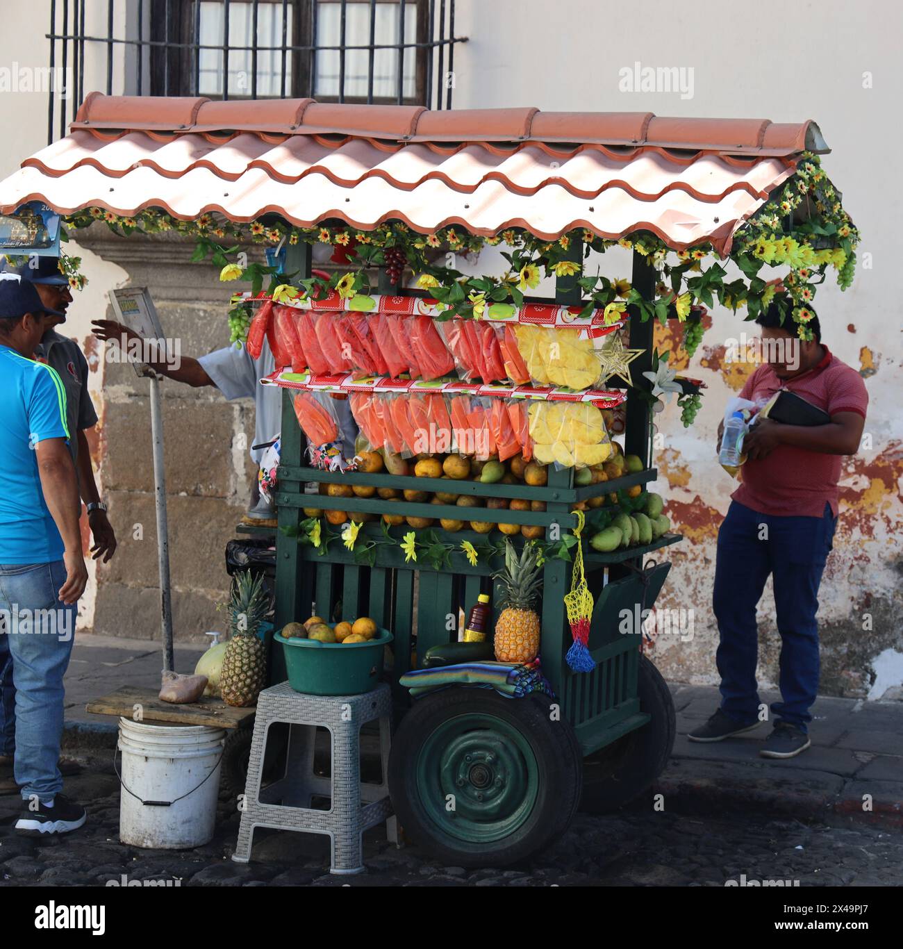 Fruit stall. Street seller, Antigua, Guatemala, Central America. Colourful street vendor's cart, selling fresh pineapple, mango, papaya, grapes etc. Stock Photo