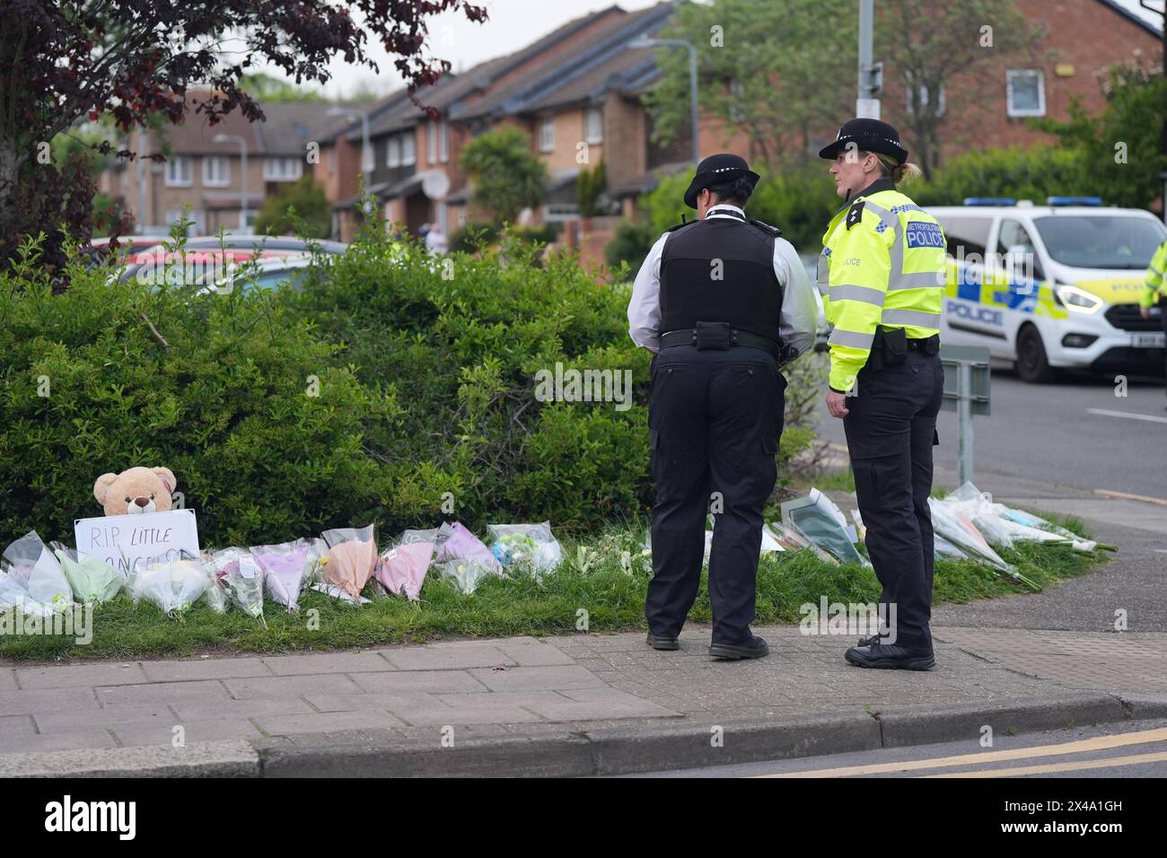 Police officers look at flowers laid on the corner of Laing Close in Hainault, north-east London, where a 14-year-old boy, named locally as Daniel Anjorin, was killed in a sword attack on Tuesday that saw four others injured, including two Metropolitan Police officers. The teenager, who was fatally injured as he walked to school in Hainault, east London, on Tuesday morning, was a pupil at the same school as Grace O'Malley-Kumar, who was stabbed to death in Nottingham last year. Picture date: Wednesday May 1, 2024. Stock Photo