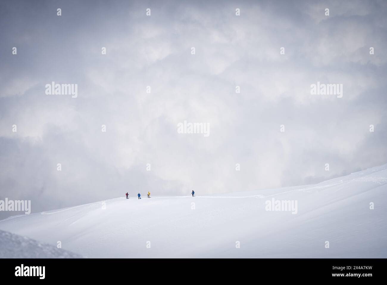 Mountaineers going down the snowy ridgeline with clouds in backdrop ...