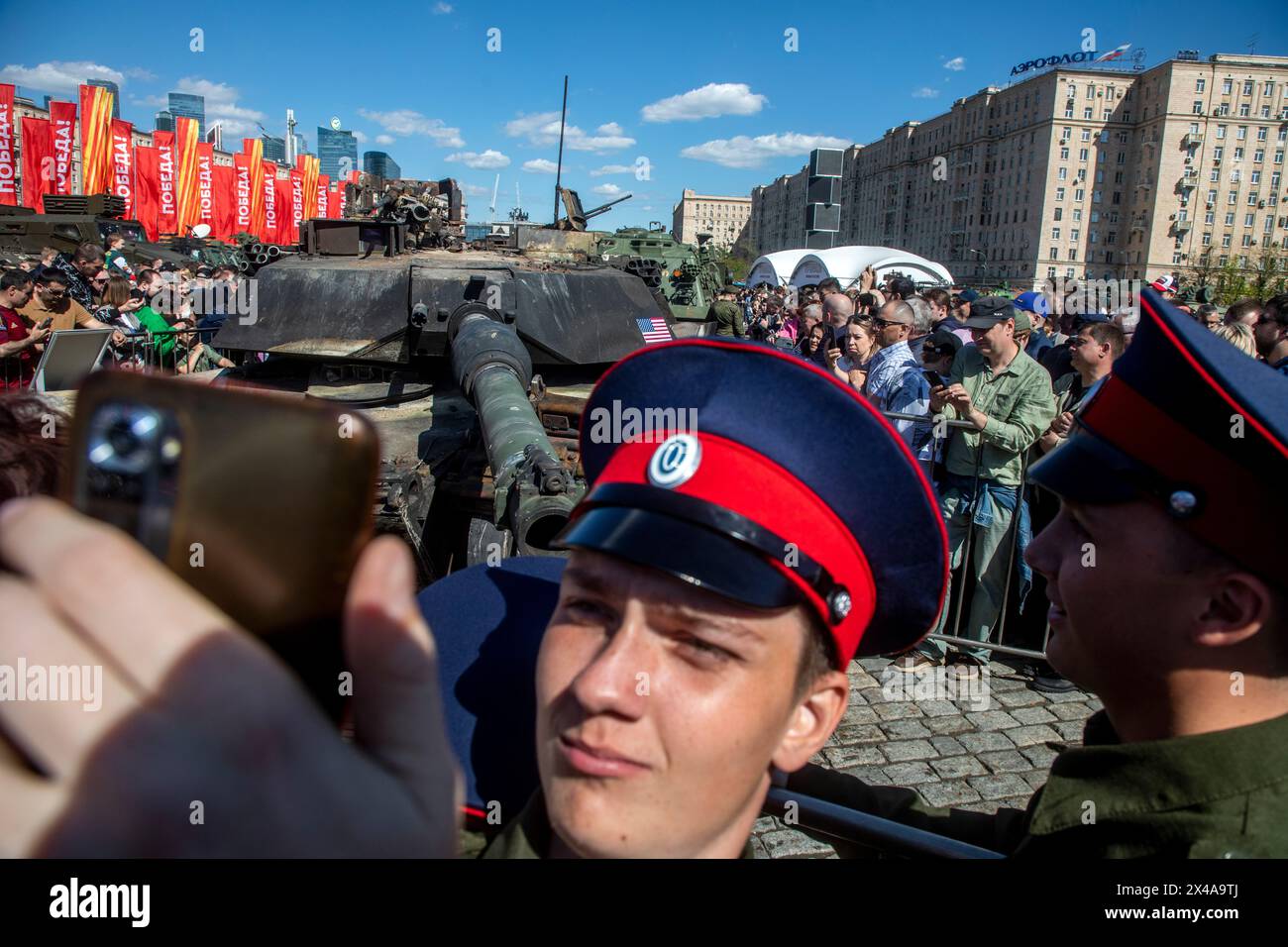 Moscow, Russia. 1st of May, 2024. Visitors look at and take photos of a U.S. made M1A1 Abrams tank, foreground, hit and captured by Russian troops during the special military operation in Ukraine which is seen on display in Moscow, Russia. An exhibition of military equipment captured from Kyiv forces during the fighting in Ukraine has opened in the Russian capital. Credit: Nikolay Vinokurov/Alamy Live News Stock Photo