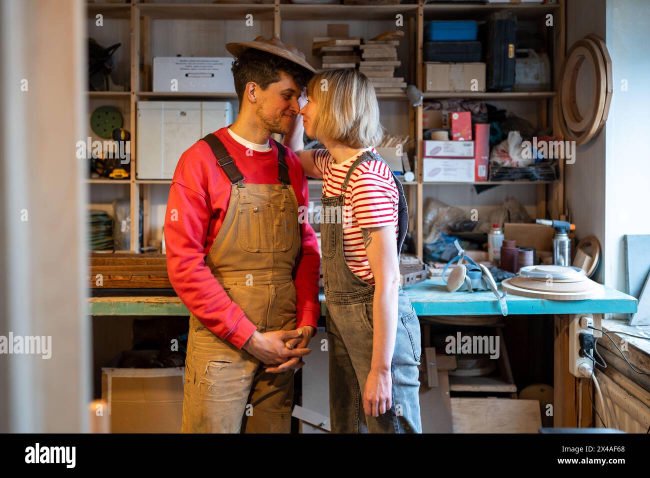 Happy couple carpenters kissing at workplace. Spouses holding hands laughing smiling expressing love Stock Photo
