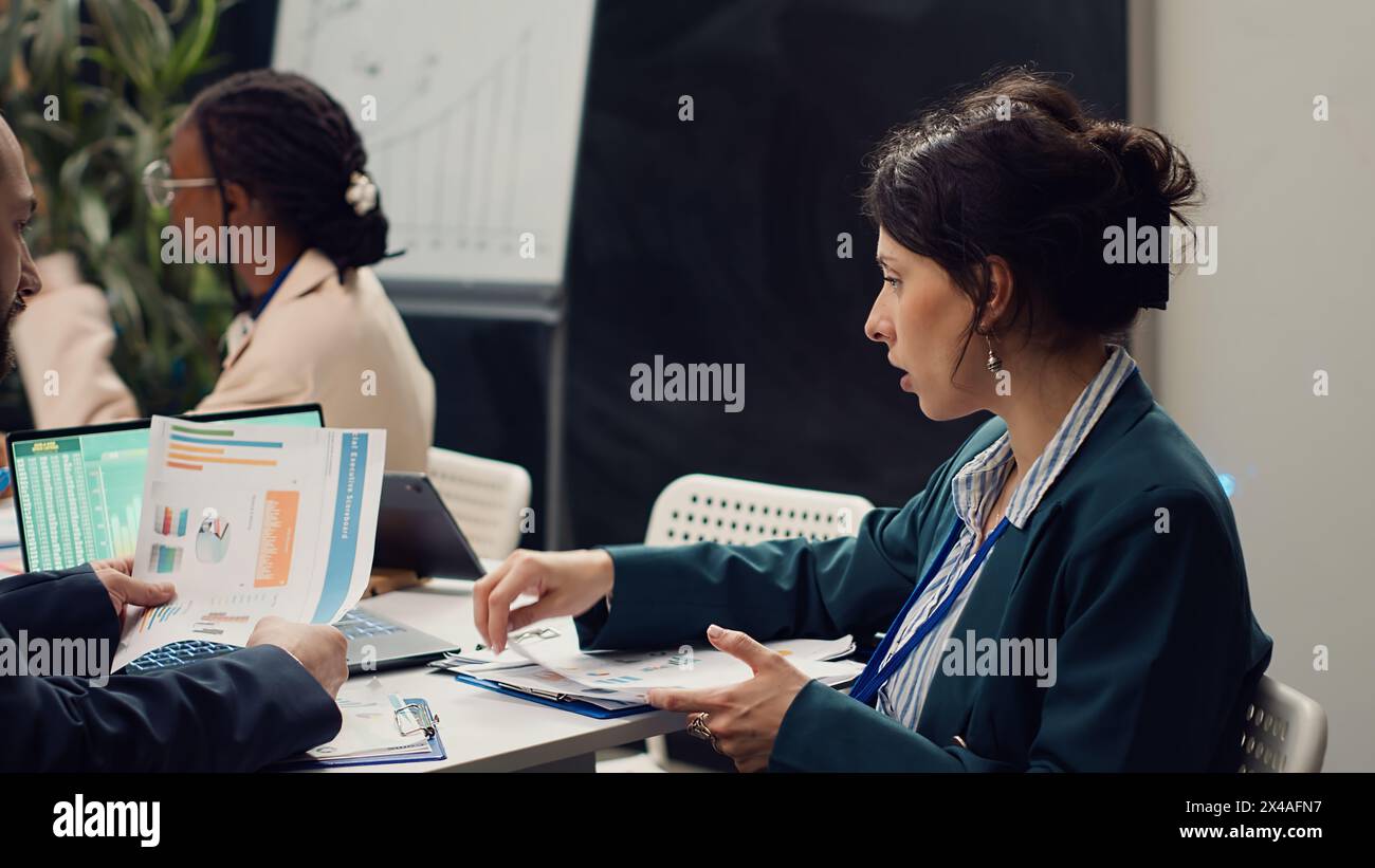 Public relations team creating marketing campaigns and promotional activities in a boardroom, collaborating on new development plan. Employees reviewing sales trends metrics on pc. Camera A. Stock Photo