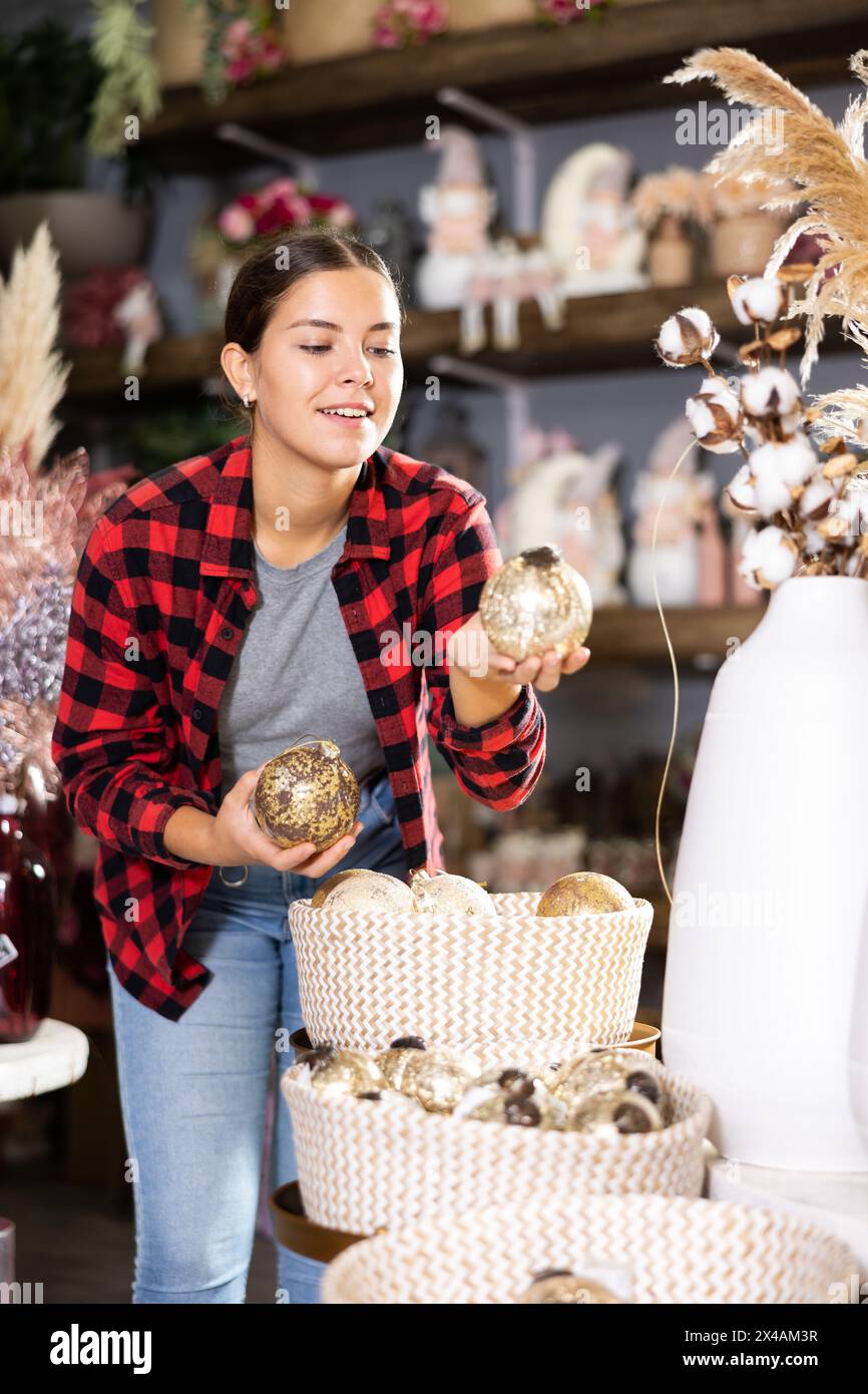 Cheerful young female in casual shirt buying Christmas bulbs before holidays in a store Stock Photo
