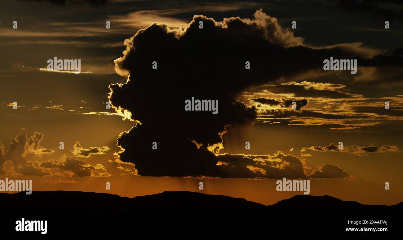 Dreamy thunderhead, beautifully silhouetted, towers above the mountainous desert landscape at sunset. Stock Photo