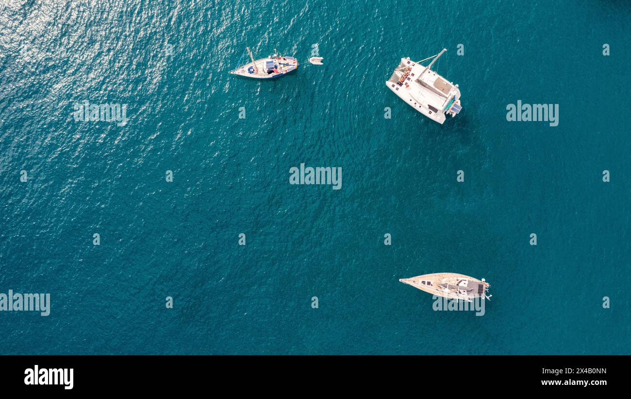 Yacht anchoring in crystal clear turquoise water in front of the tropical island, alternative lifestyle, living on a boat. Aerial view of yacht at anc Stock Photo