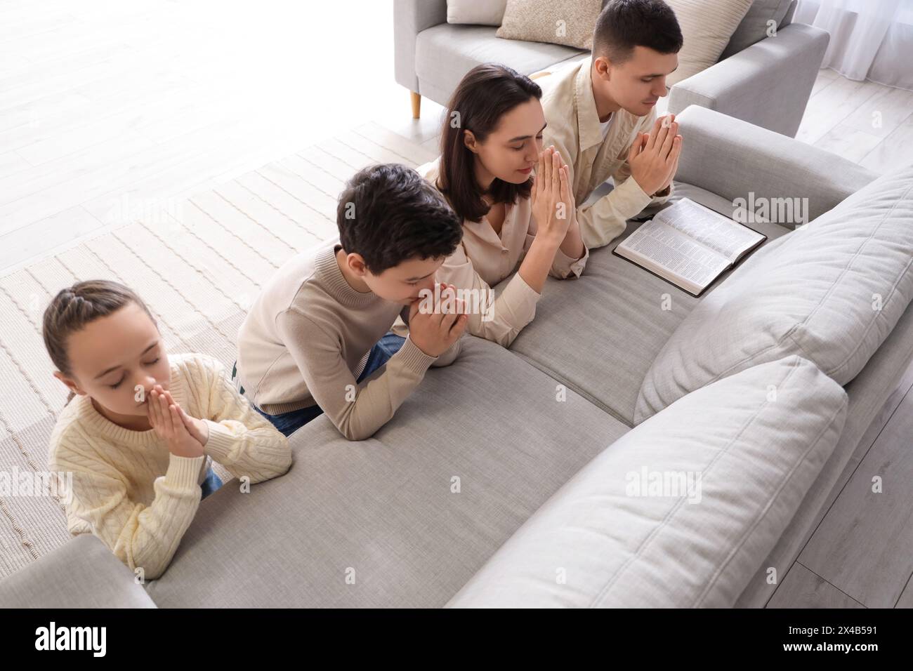 Family with Holy Bible praying behind sofa at home Stock Photo