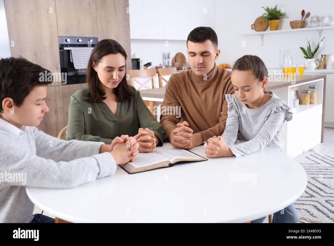 Family praying with Holy Bible on table in kitchen Stock Photo