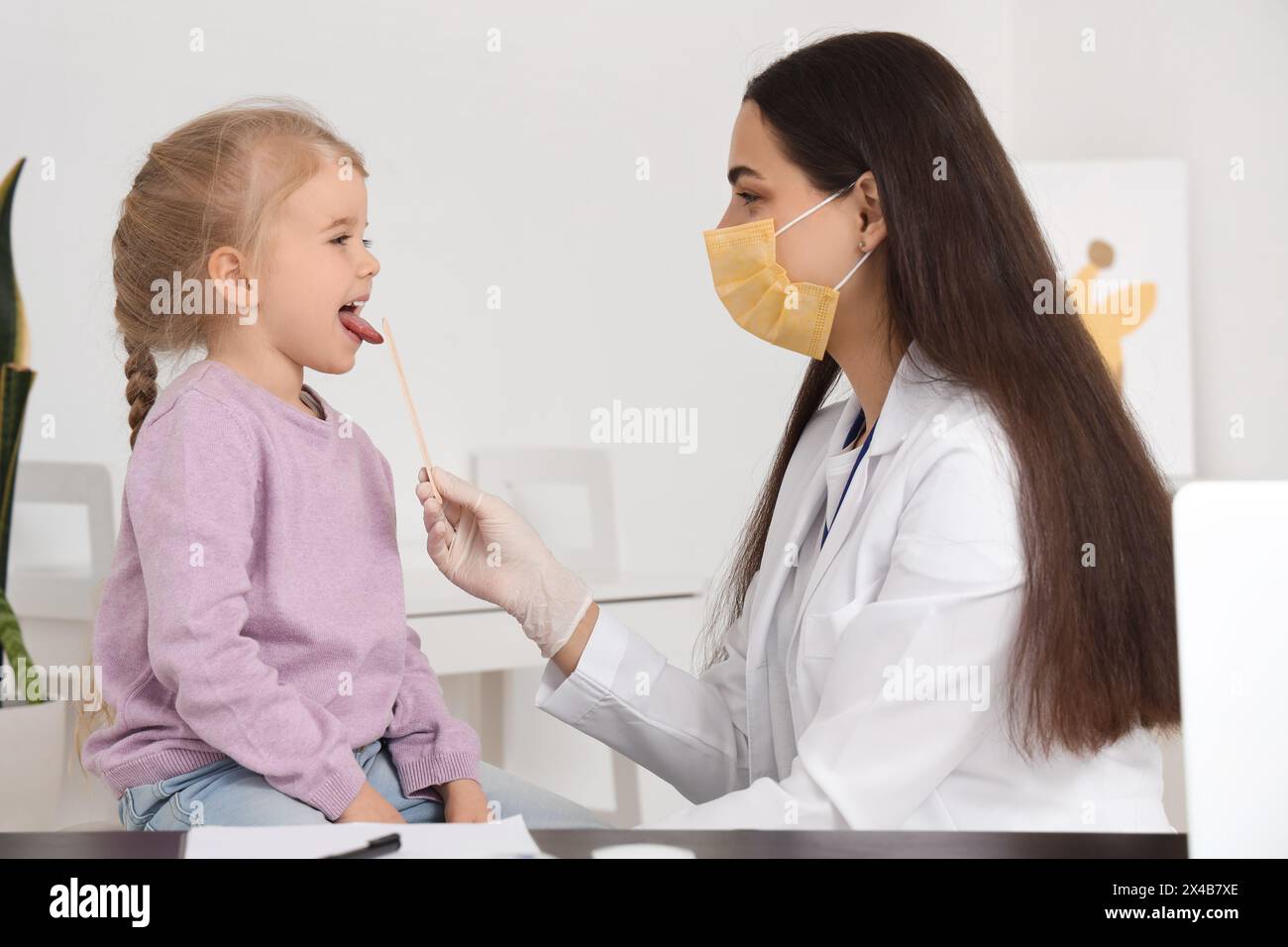 Female pediatrician examining little girl's throat with tongue
