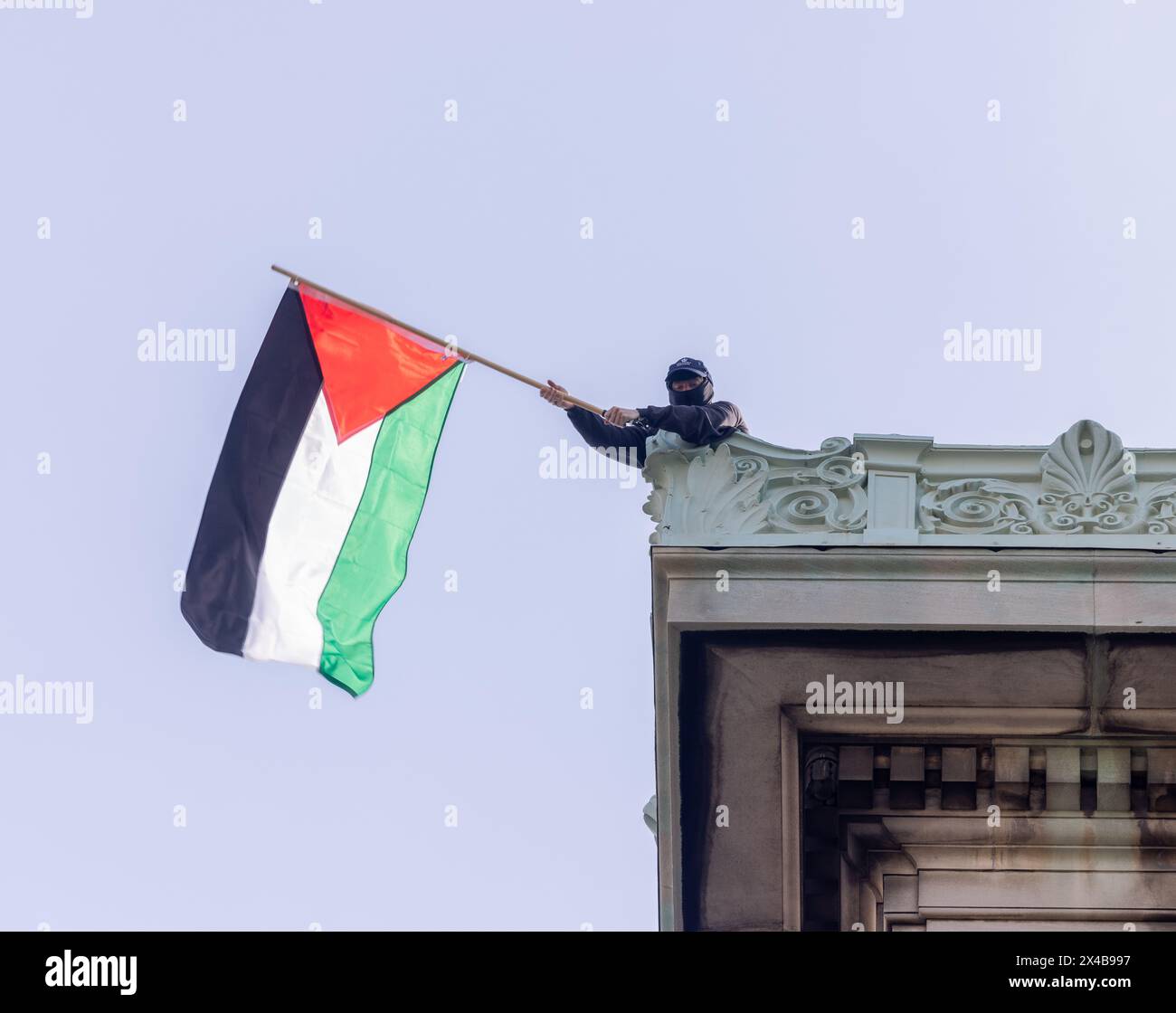NEW YORK, N.Y. – April 30, 2024: A demonstrator waves a Palestinian flag on the roof of Hamilton Hall at Columbia University in Manhattan. Stock Photo