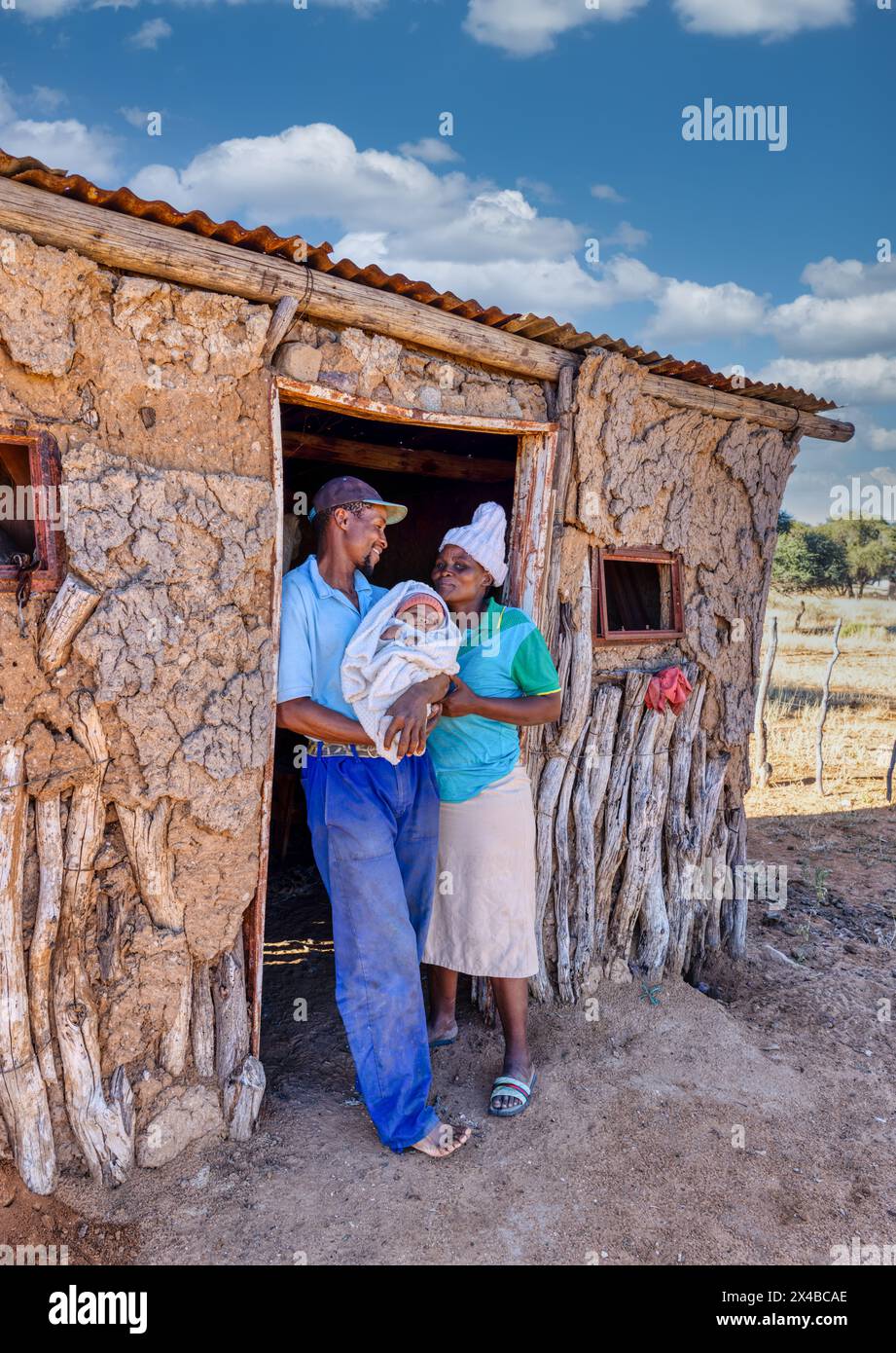 african village, single african father and mother holding the baby standing in front of the mud house in the village Stock Photo