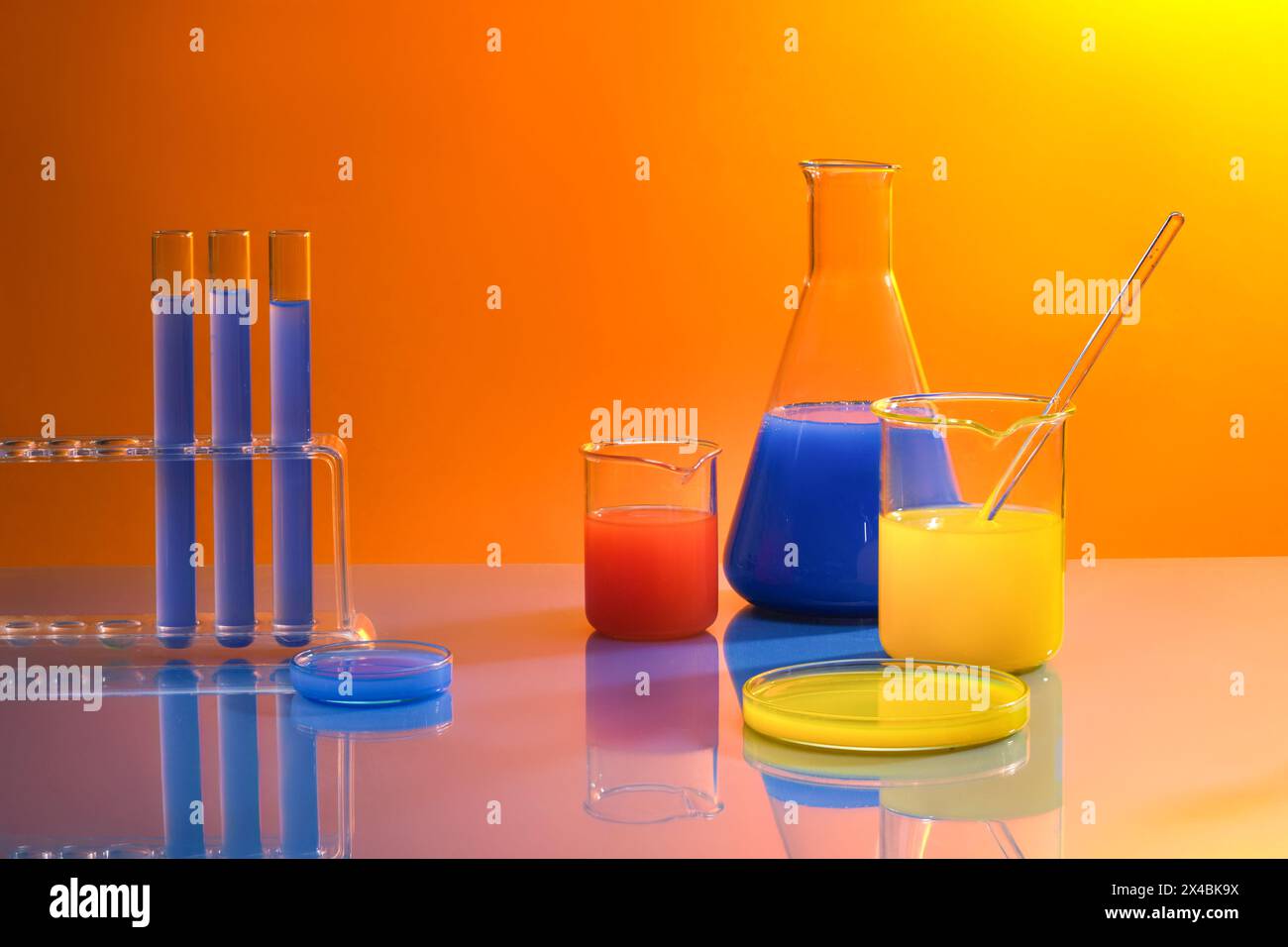 Advertising scene with laboratory equipments - test tubes, erlenmeyer flask, beakers and petri dish with colorful liquid inside decorated on orange gr Stock Photo