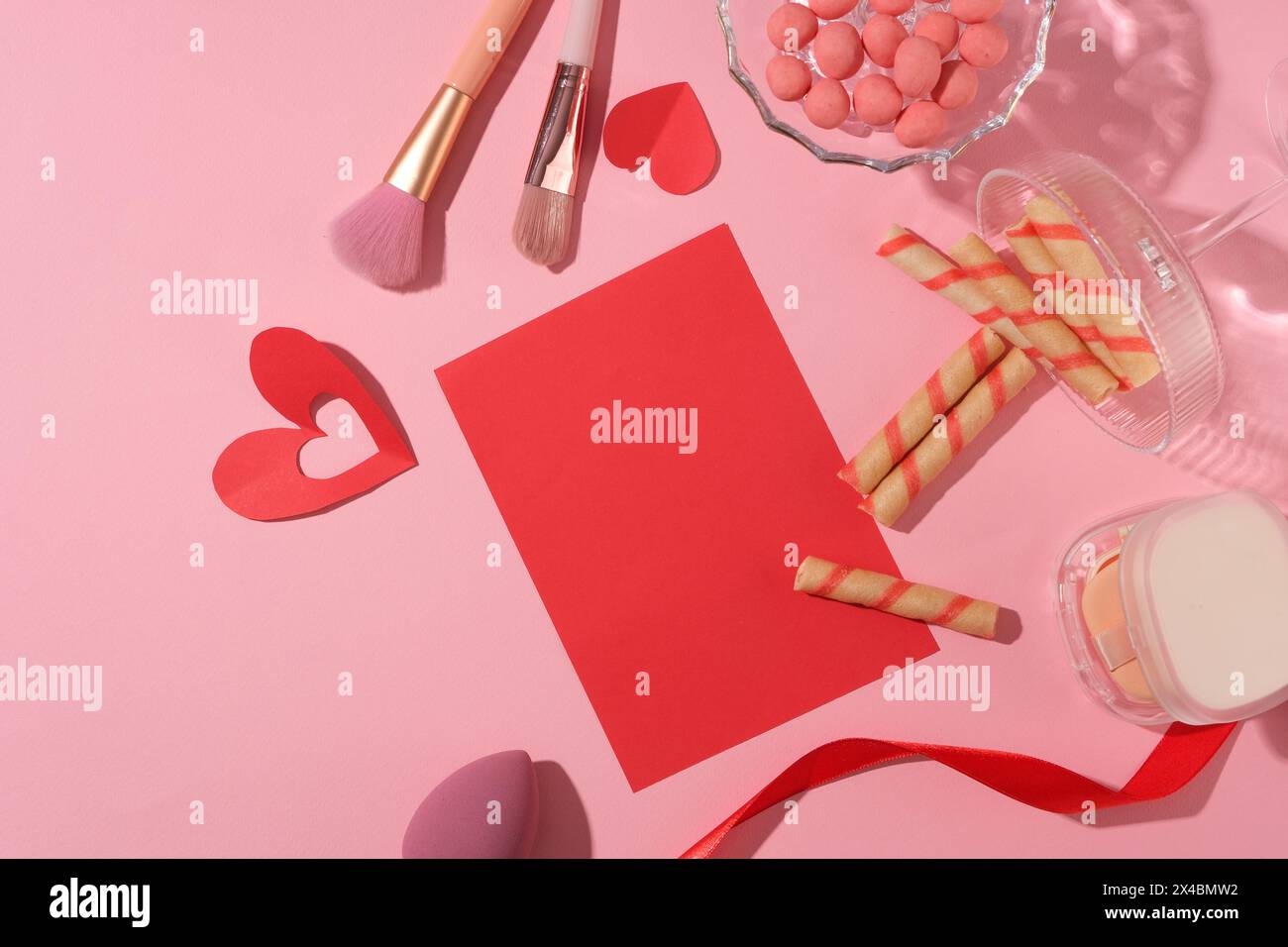 Decorate Valentine's cards with makeup and sweet cakes. Red paper plate with cake, chocolate, cushion and makeup brush on pink background. Top view an Stock Photo