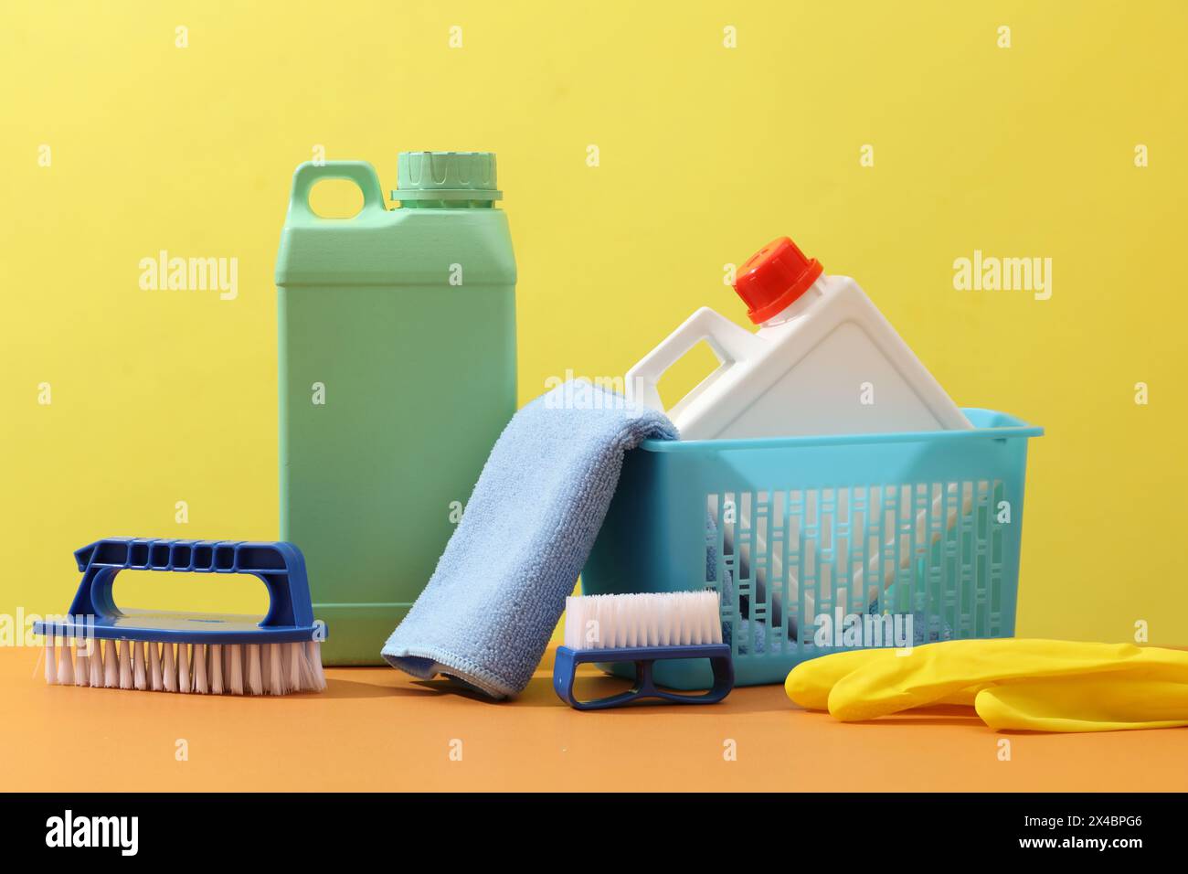 Cleaning tools displayed on a yellow background with blank canisters mockup for detergent product, wiper, brushes and gloves. Front view, empty place Stock Photo