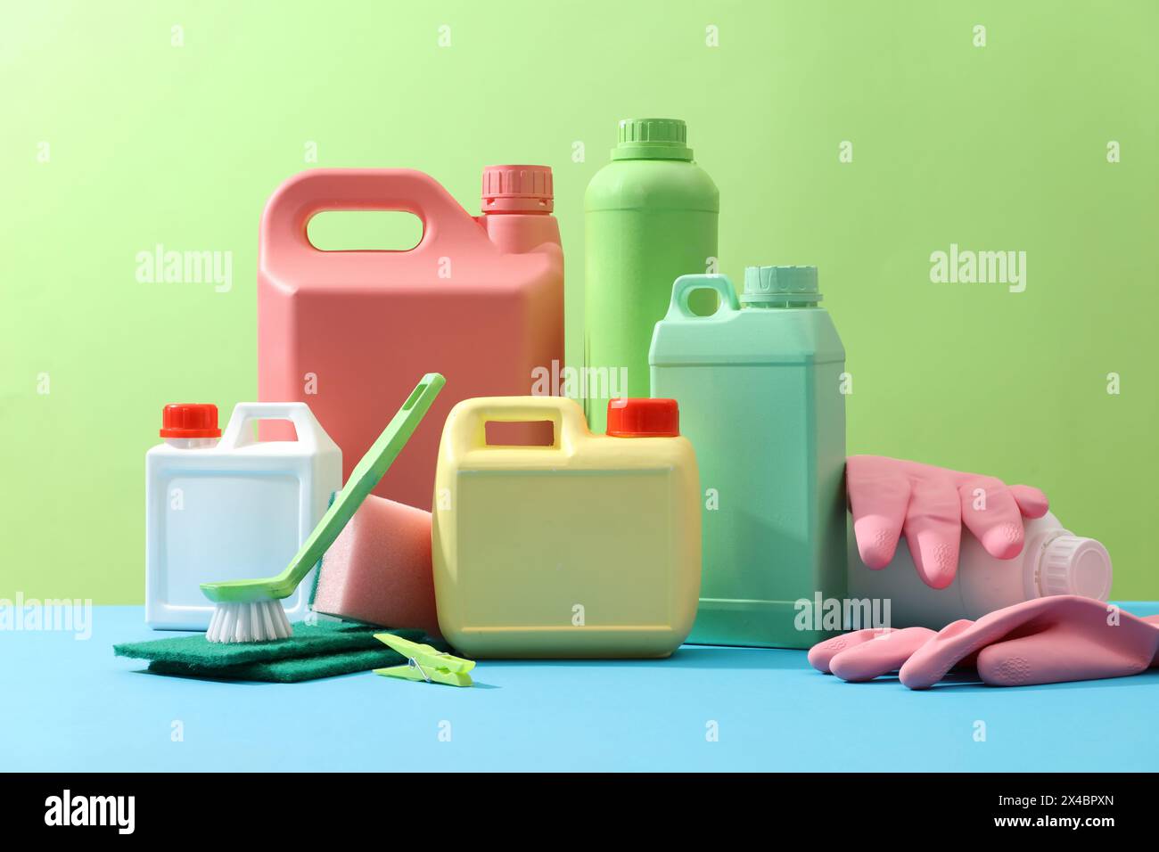 Cleaning products placed on a green background with empty bottles mockup for detergent product, rubber gloves, brushes and sponges. Creative ideas for Stock Photo